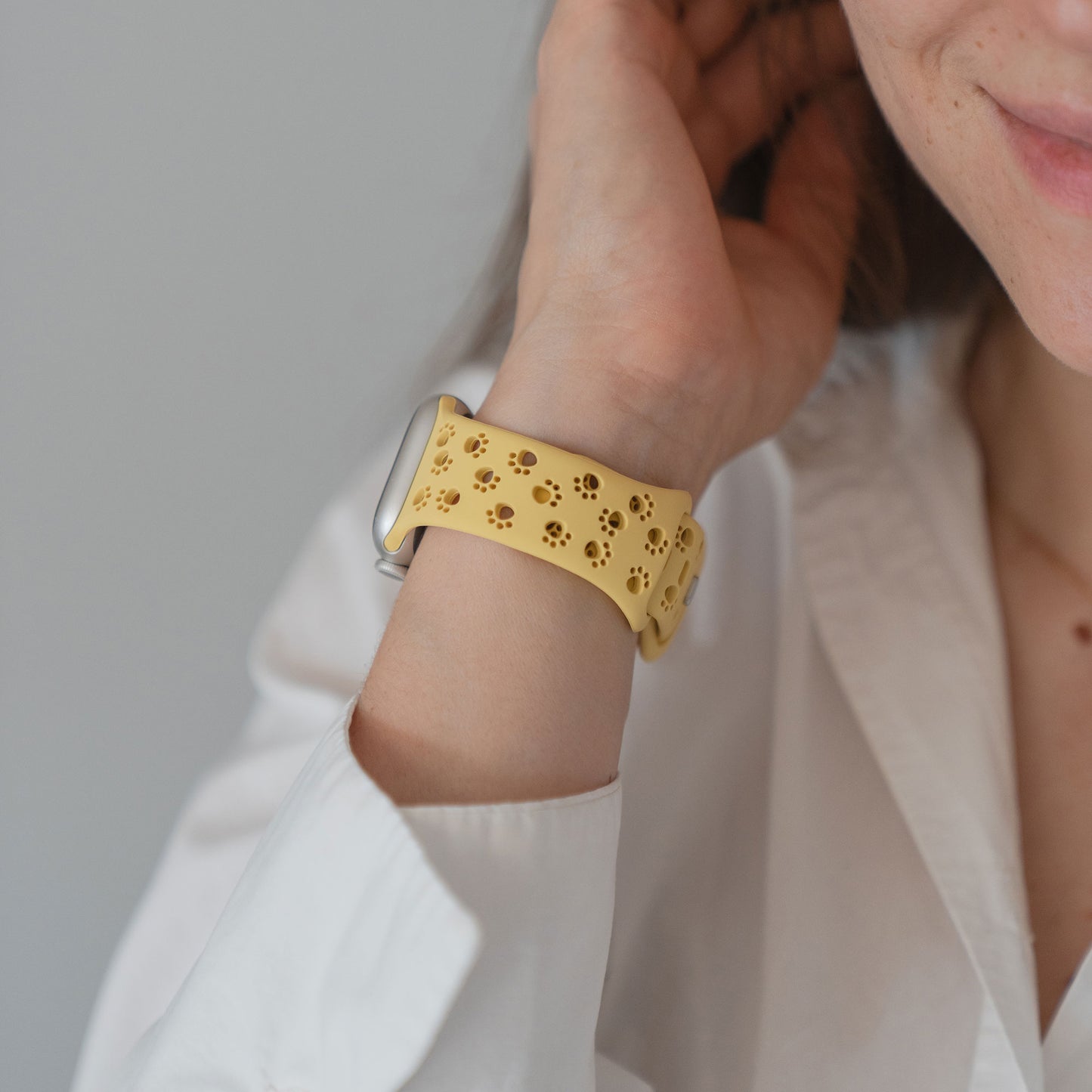 Person in einem weißen Hemd, die ein Arktisband Apple Watch Silikonarmband "Paw" mit einem floralen Ausschnitt in Gelb trägt und ihr Haar berührt.