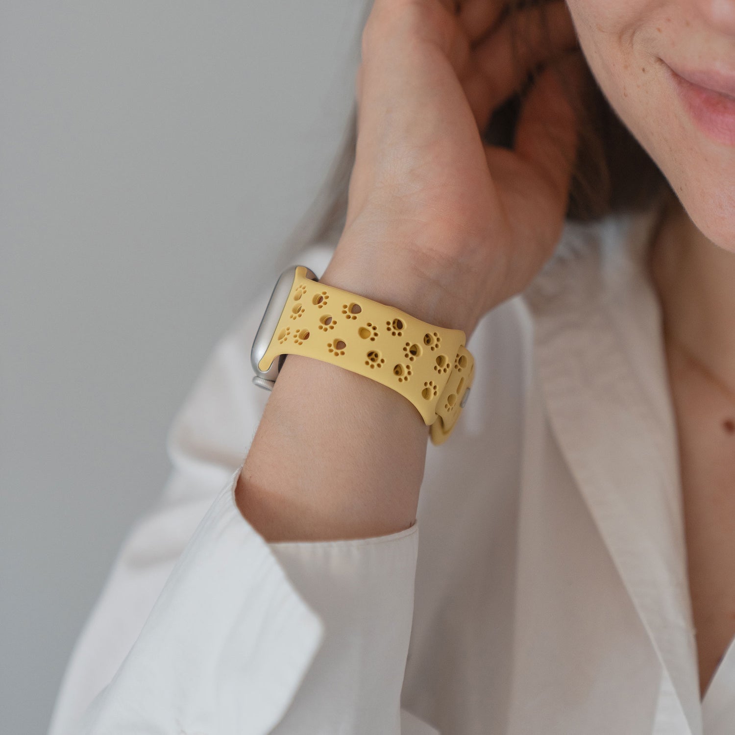 Person in einem weißen Hemd, die ein Arktisband Apple Watch Silikonarmband "Paw" mit einem floralen Ausschnitt in Gelb trägt und ihr Haar berührt.