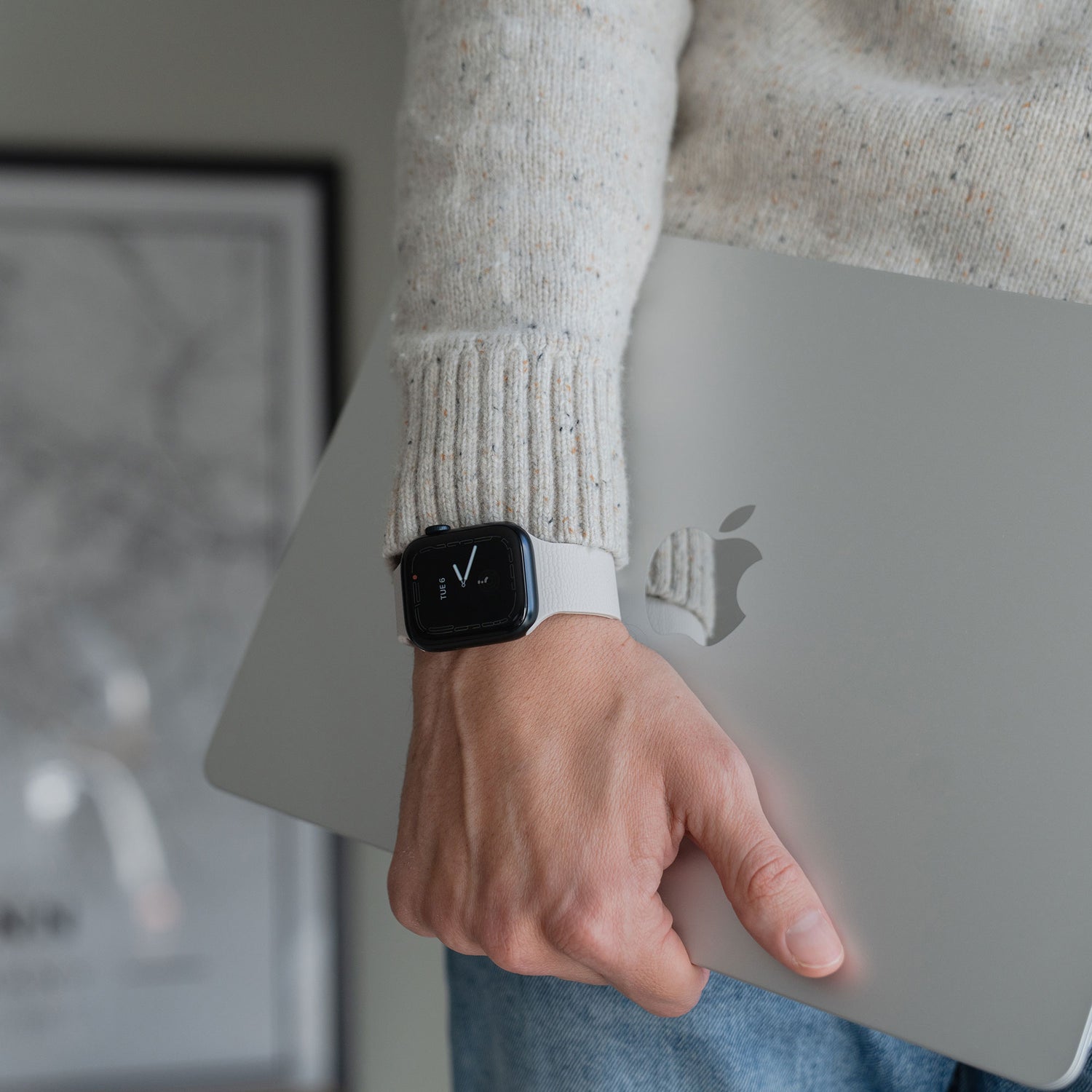 Eine Person trägt ein arktisband Apple Watch magnetisches Silikonarmband "Flexy" von arktisband, hält ein geschlossenes MacBook und hat einen Pullover an.