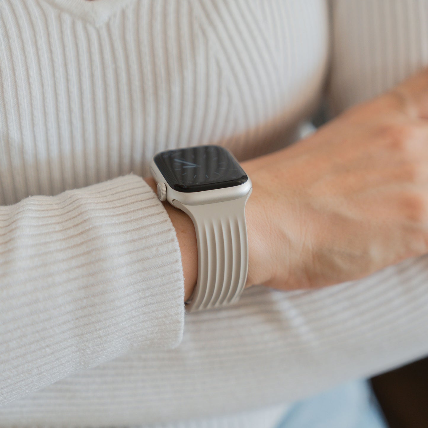 Eine Person, die das arktisband Apple Watch Armband "Skandi" mit einem Fluorelastomer-Band und einem gerippten, weißen, langärmeligen Skandi-Top trägt, mit verschränkten Armen.