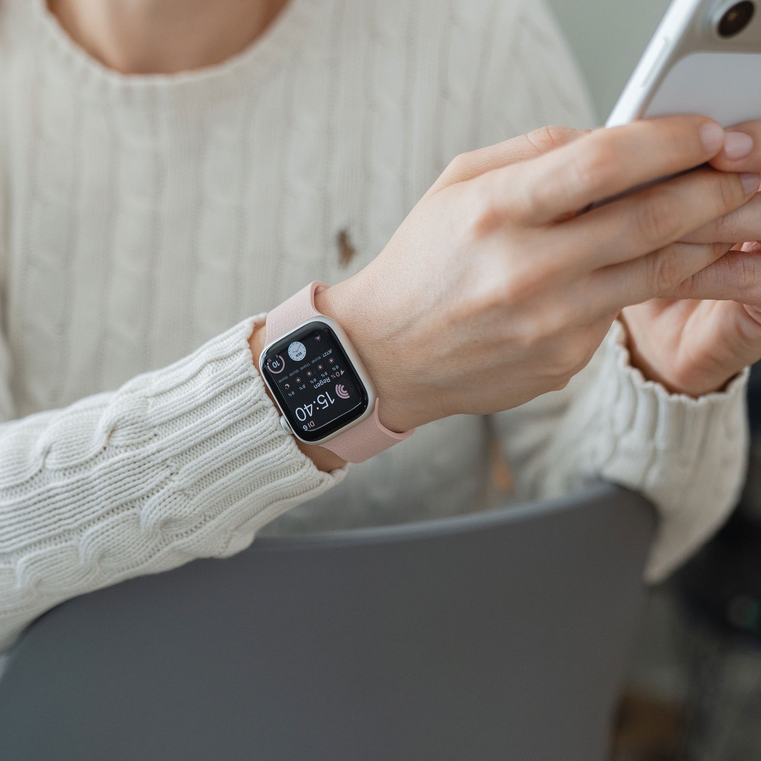 Person in einem weißen Pullover, die ein Smartphone benutzt, trägt ein Arktisband Apple Watch magnetisches Silikonarmband "Flexy" in rosa an ihrem Handgelenk.