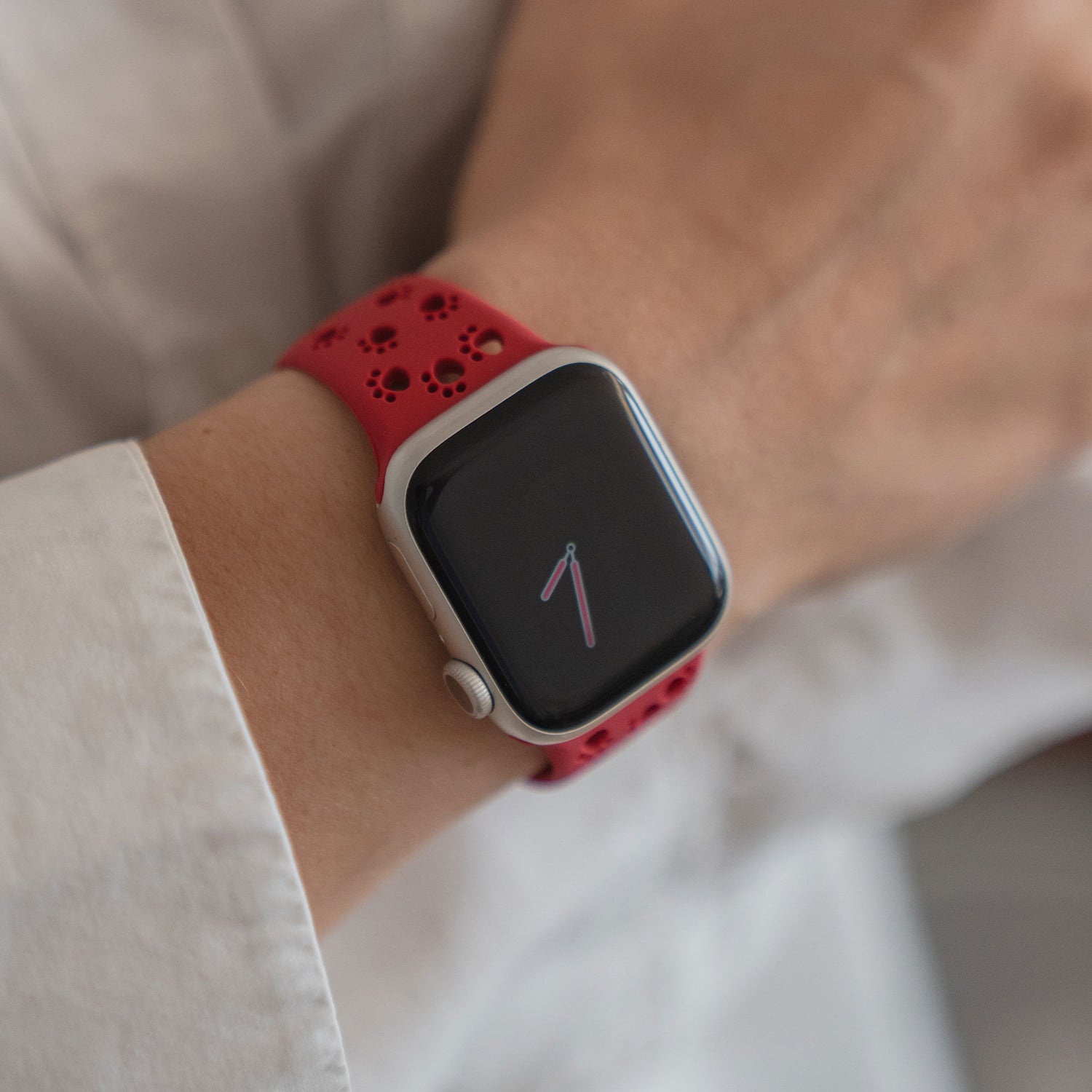 Eine Person trägt ein arktisband Apple Watch Silikonarmband "Paw" von arktisband in rot, das die Uhrzeit am Handgelenk anzeigt.