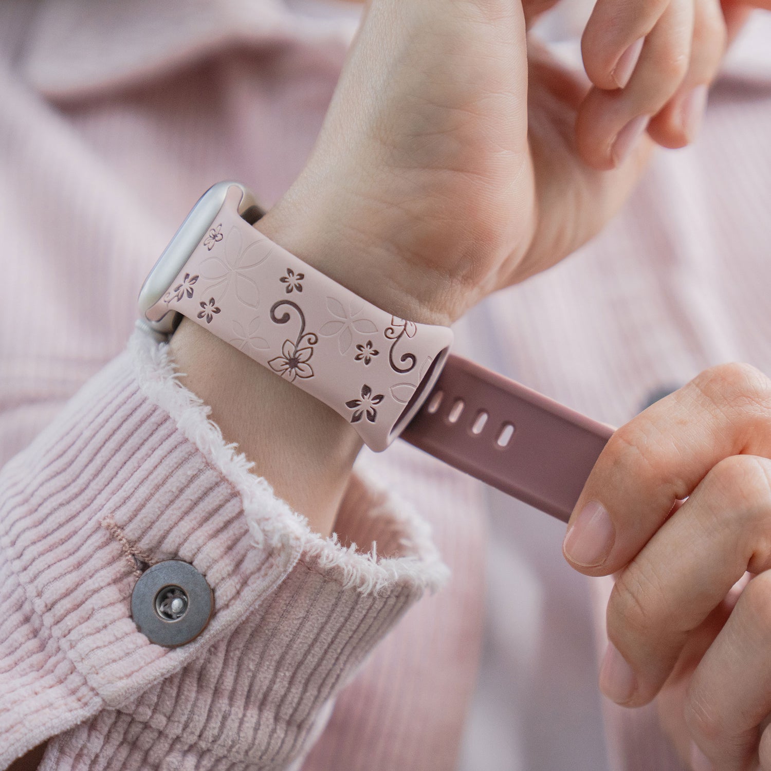 Nahaufnahme einer Person, die ein rosa Hemd trägt und ein arktisband Apple Watch Silikonarmband "Bloom" von arktisband mit einem Blumenmuster an ihrem Handgelenk befestigt.