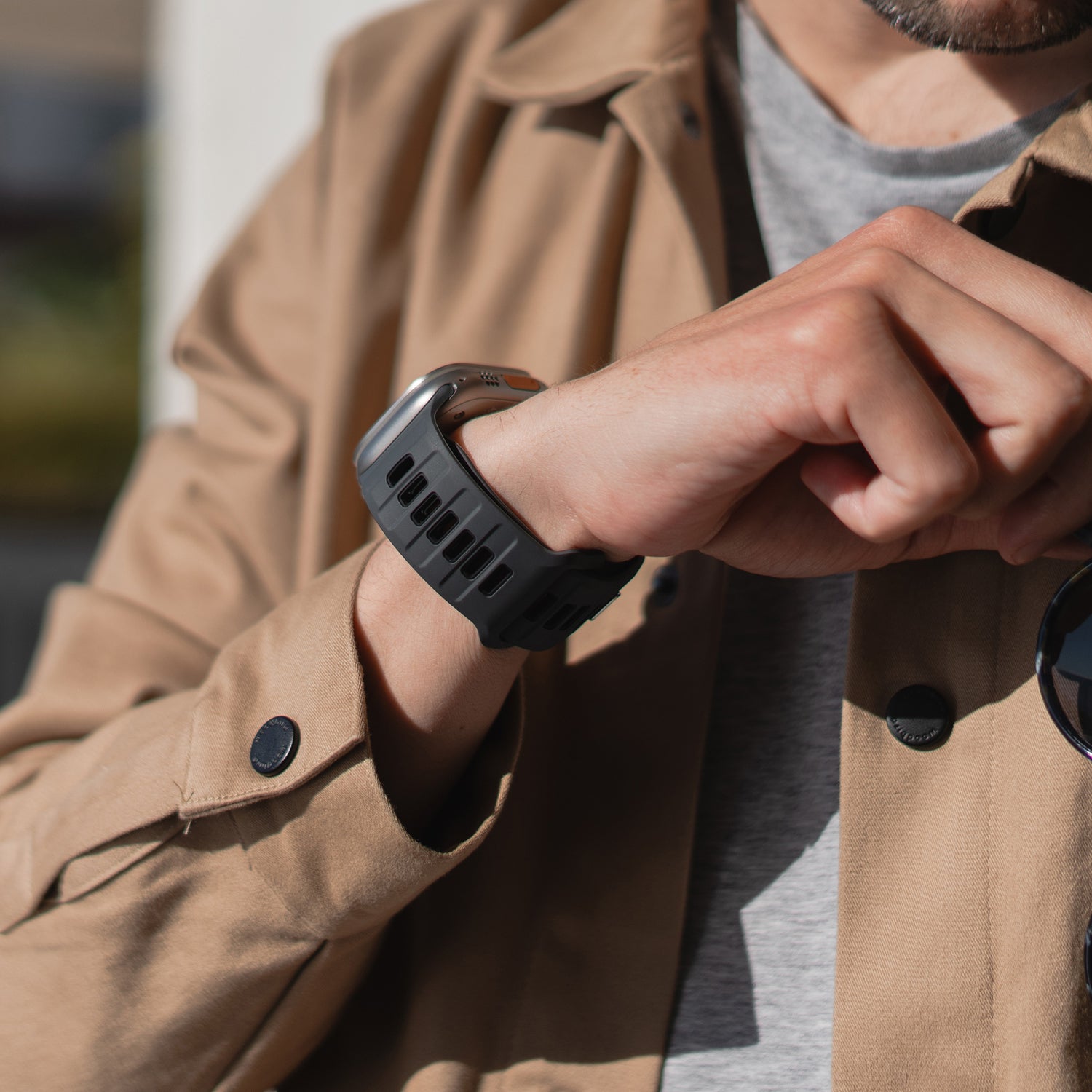 Eine Person in hellbrauner Jacke und grauem Hemd betrachtet ein arktisband Apple Watch Silikonarmband „Runner“ von arktisband mit atmungsaktiver Bandstruktur an ihrem linken Handgelenk und berührt es mit der rechten Hand. Ihr Gesicht ist teilweise sichtbar.