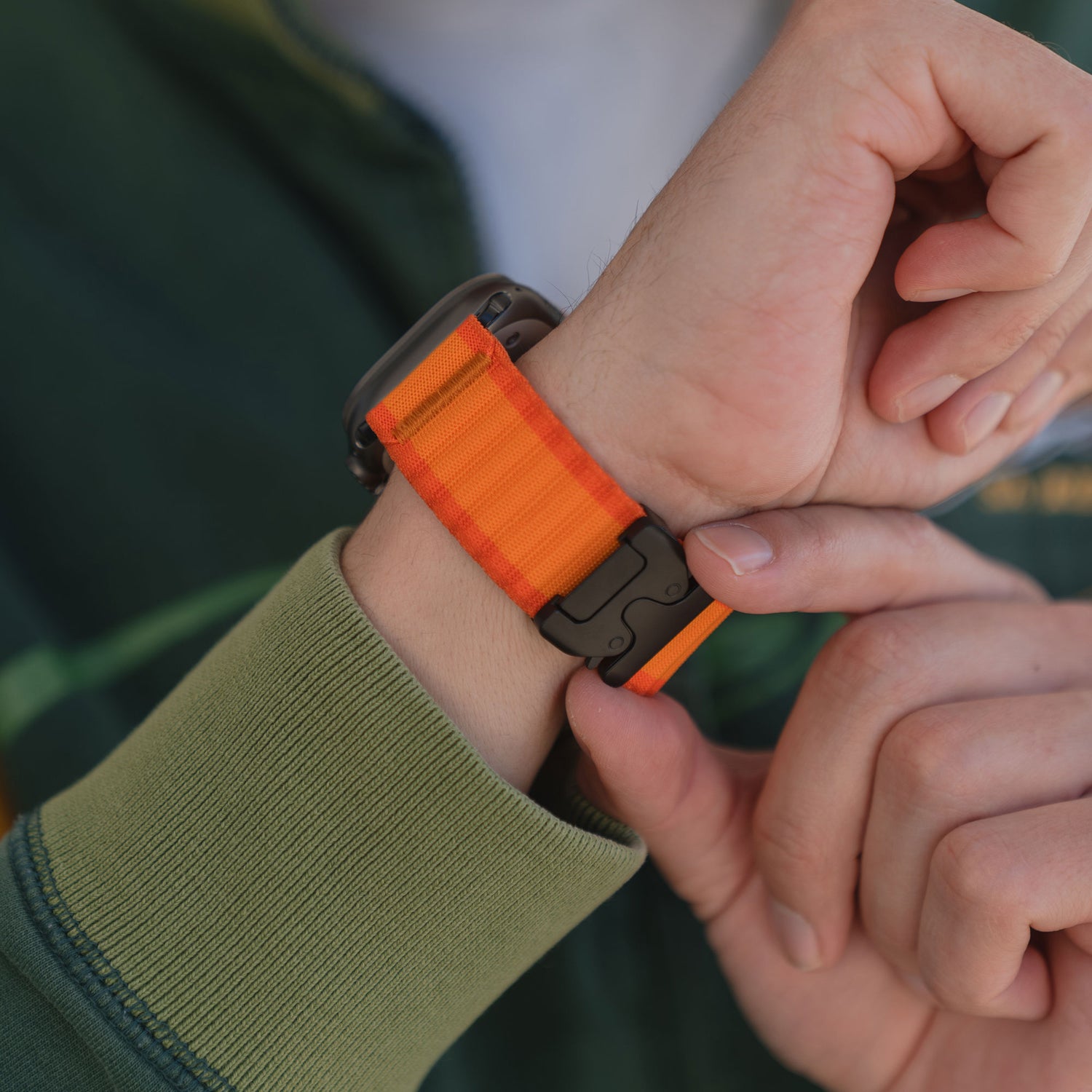 Eine Person befestigt ein orange-gestreiftes Arktisband Apple Watch Armband "CoreX" mit einem sicheren Parachute-Verschluss an ihrem Handgelenk.