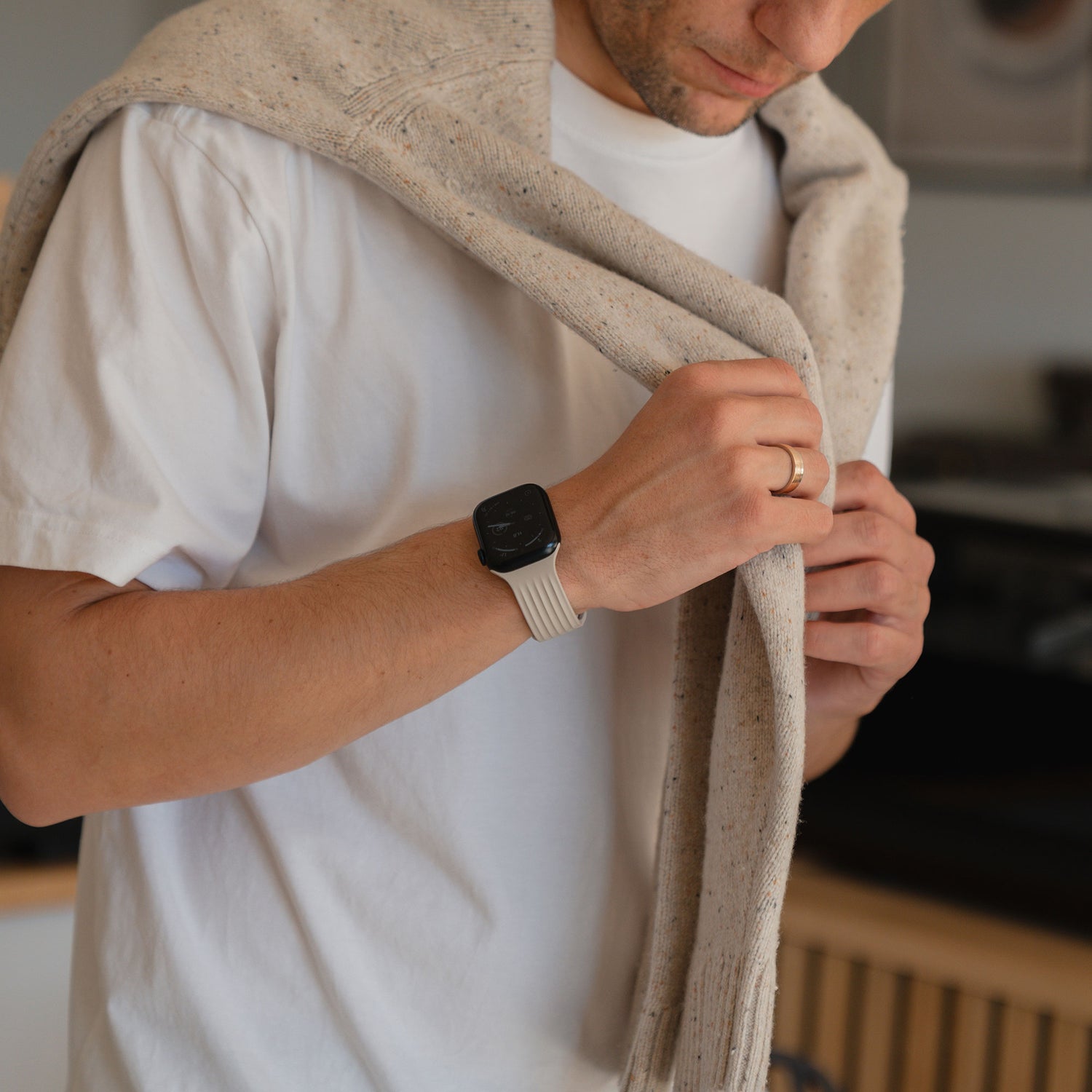 Mann mit weißem T-Shirt und arktisband Apple Watch Armband "Skandi" von arktisband, mit einem über die Schultern gezogenen Pullover, den er verstellt - eine Mischung aus Skandi-Stil und smarten Accessoires.