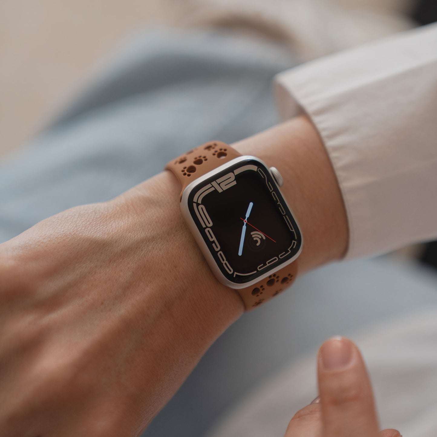 Eine Person trägt ein Arktisband Apple Watch Silikonarmband "Paw" mit einem hellbraunen Band mit Pfotenabdrücken und berührt den Bildschirm der Uhr.