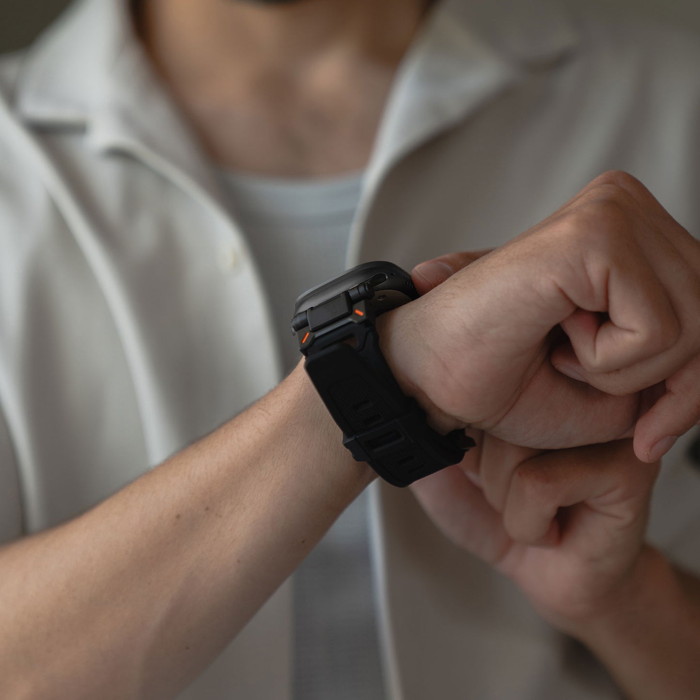 Eine Person in einem kurzärmeligen weißen Hemd rückt ein arktisband Apple Watch Ultra Armband „Atlas“ von arktisband mit orangefarbenen Akzenten und eckigem Design an ihrem linken Handgelenk zurecht. Das Gesicht der Person ist nicht zu sehen.