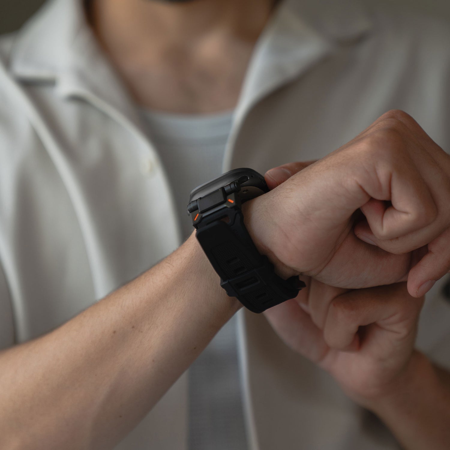 Eine Person in einem kurzärmeligen weißen Hemd rückt ein arktisband Apple Watch Ultra Armband „Atlas“ von arktisband mit orangefarbenen Akzenten und eckigem Design an ihrem linken Handgelenk zurecht. Das Gesicht der Person ist nicht zu sehen.