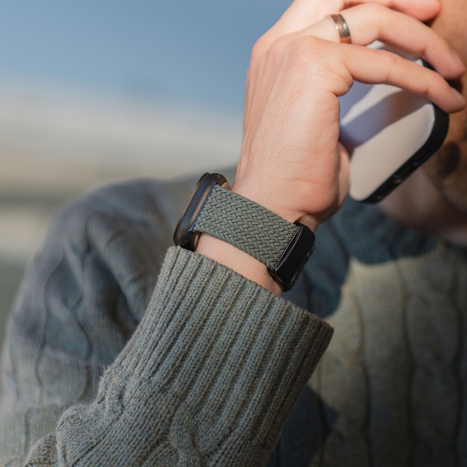 Eine Person in einem Strickpullover trägt ein „Geflochtenes Apple Watch Ultra Armband ‚Casual‘ mit Magnetverschluss“ von arktisband und hält sich beim Telefonieren ein Smartphone ans Ohr.