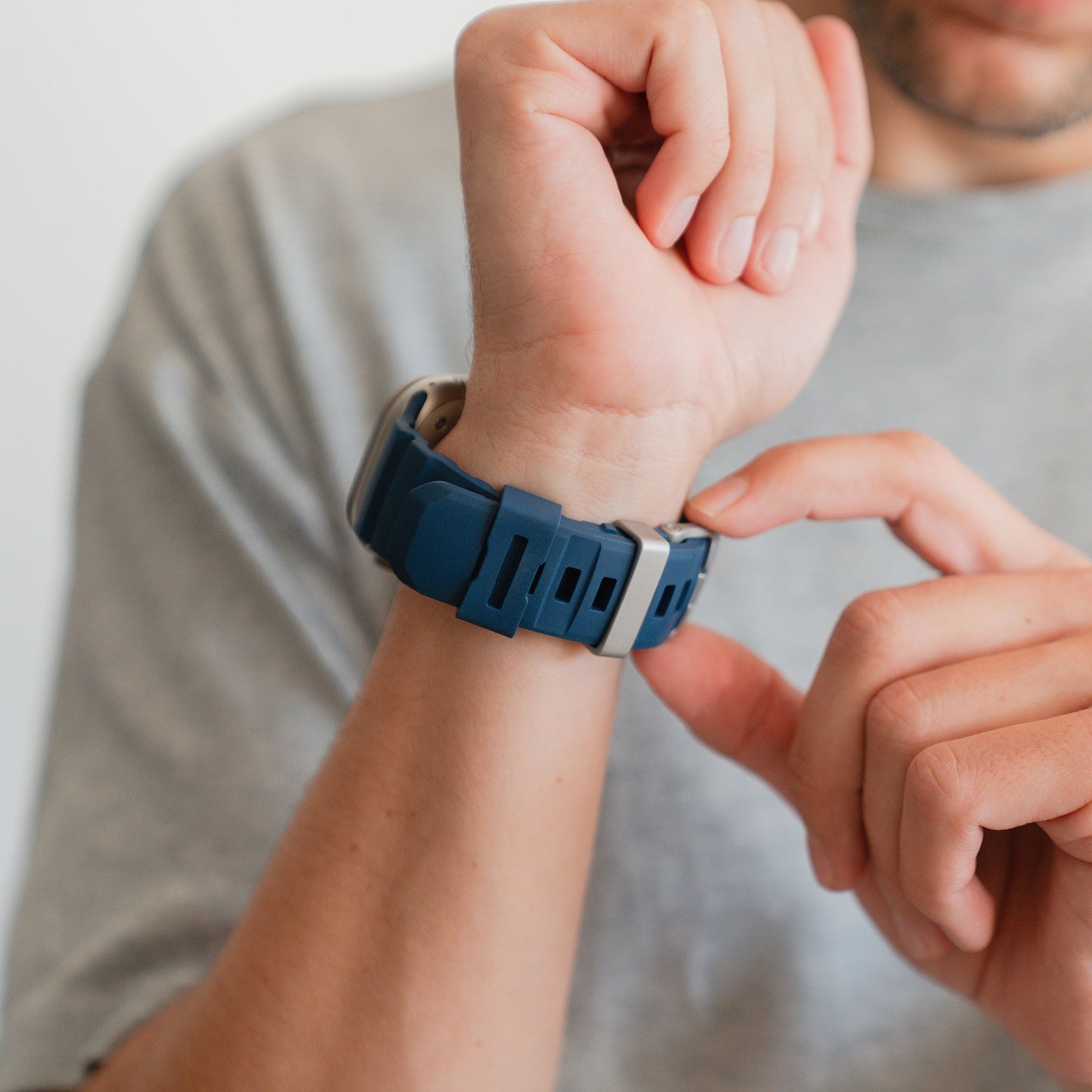 Eine Person passt das blaue Arktisband Apple Watch Armband "Flux" mit Edelstahl Schließe an ihrem linken Handgelenk an, sie trägt ein graues Hemd.