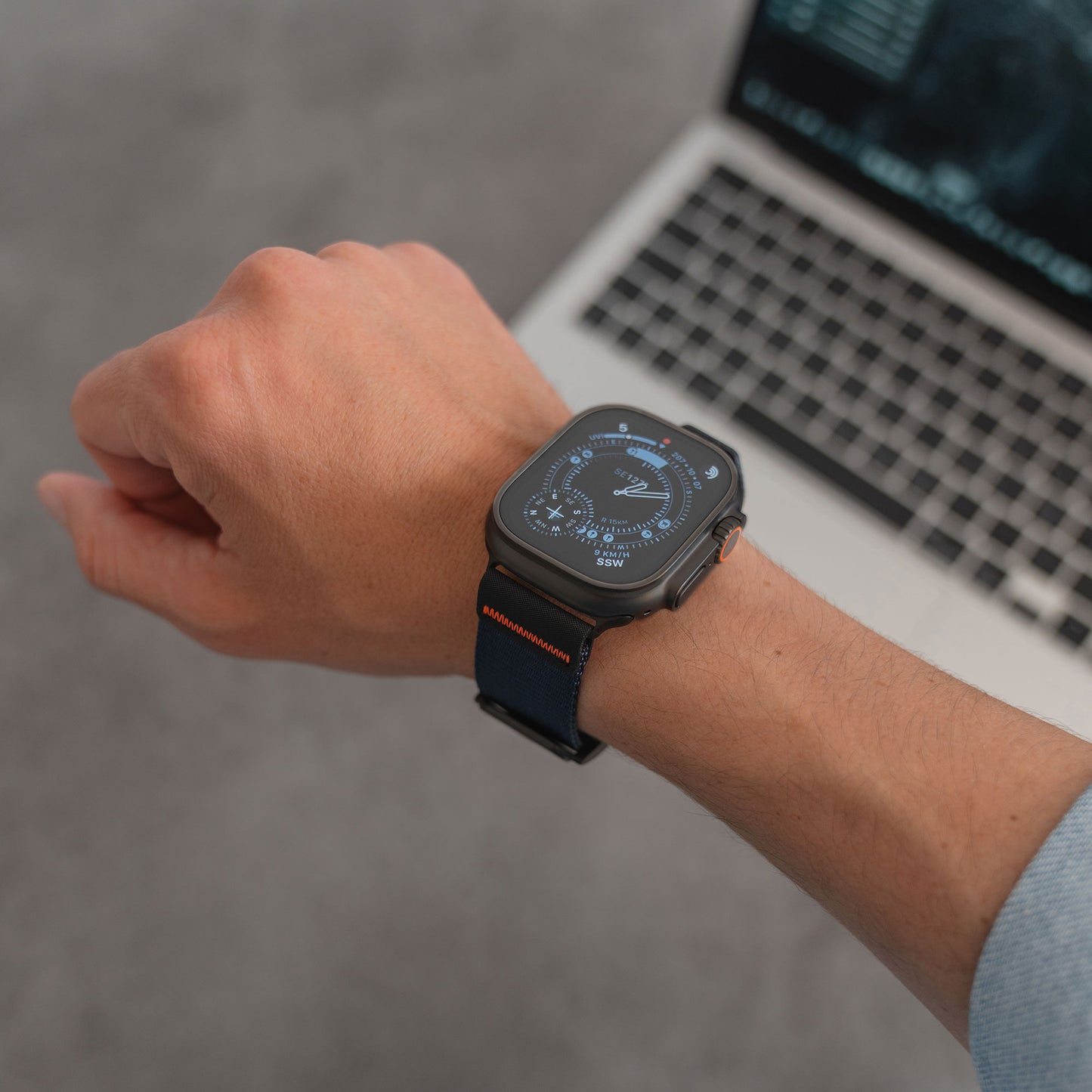 Jemand, der ein arktisband Apple Watch Armband "Terra" von arktisband mit einem blauen extrabreiten 24-mm-Nylon-Outdoor-Band trägt, arbeitet im Hintergrund an einem Laptop.