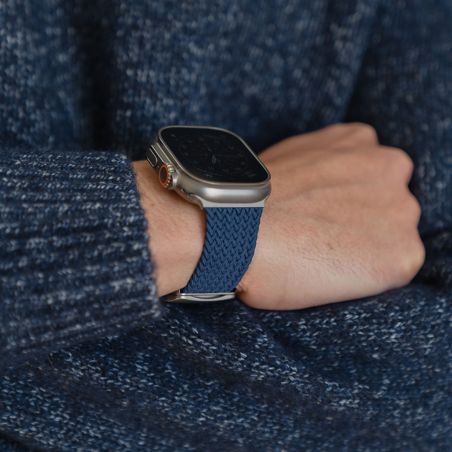 Eine Person, die ein „Geflochtenes“ Apple Watch Ultra-Armband „Casual“ von arktisband mit blauem Magnetverschluss und einen blauen Strickpullover trägt.
