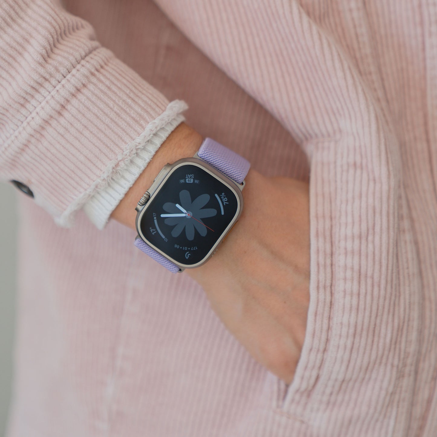 Eine Person in einer rosa Jacke trägt ein Arktisband Apple Watch Nylonarmband "FlexOne" in Lila am linken Handgelenk, die Hand in der Tasche.