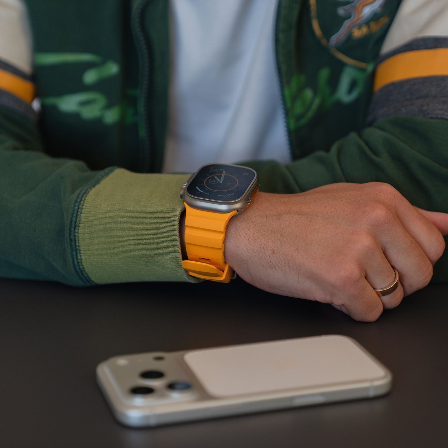 Eine Person, die ein arktisband Apple Watch Armband "Flux" mit gelbem FKM-Band und Edelstahl Schließe trägt, sitzt an einem Tisch und hat ein Smartphone vor sich liegen.