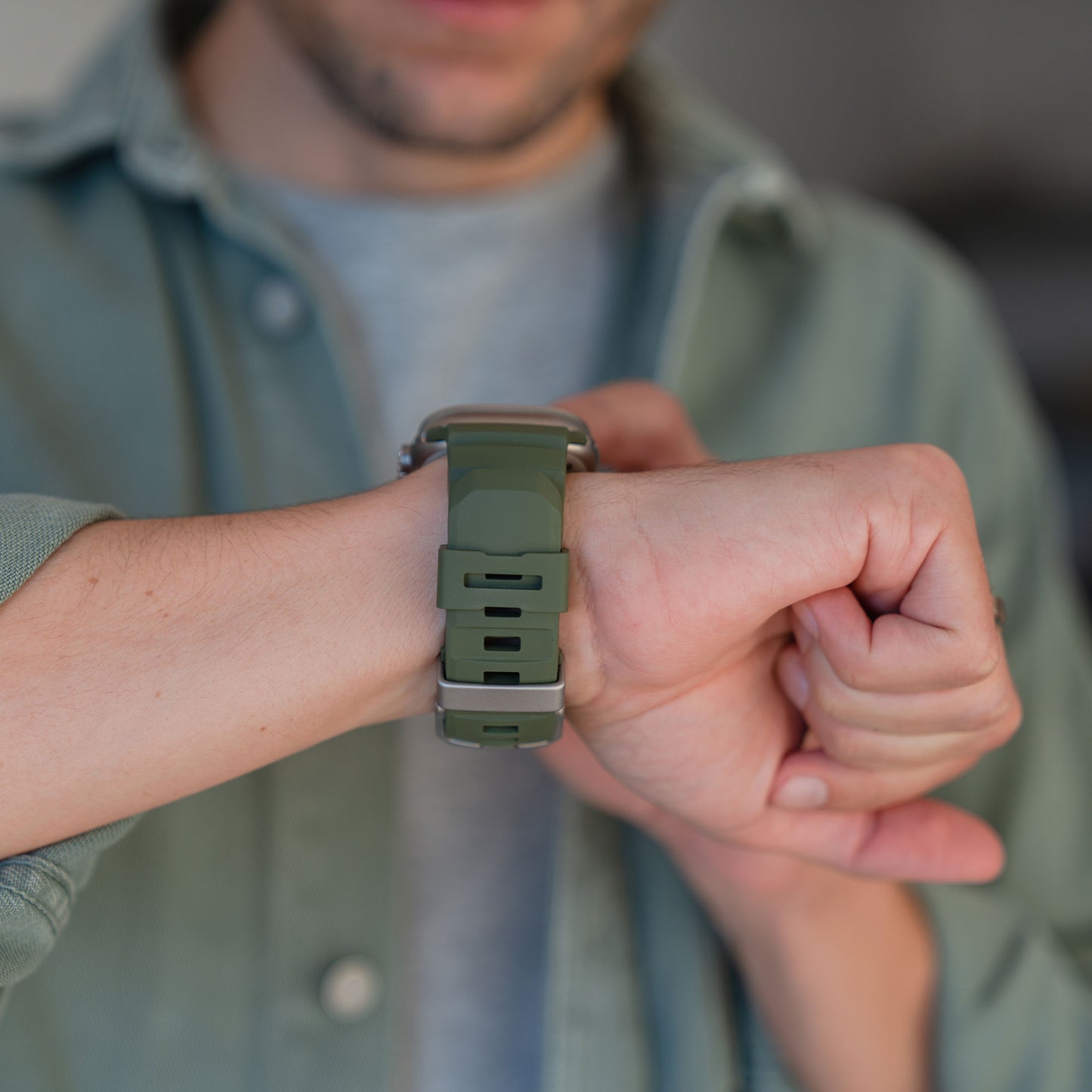 Eine Person trägt ein grünes Arktisband Apple Watch Armband "Flux" mit Edelstahl-Schließe und berührt ihr Handgelenk, während sie es ansieht.