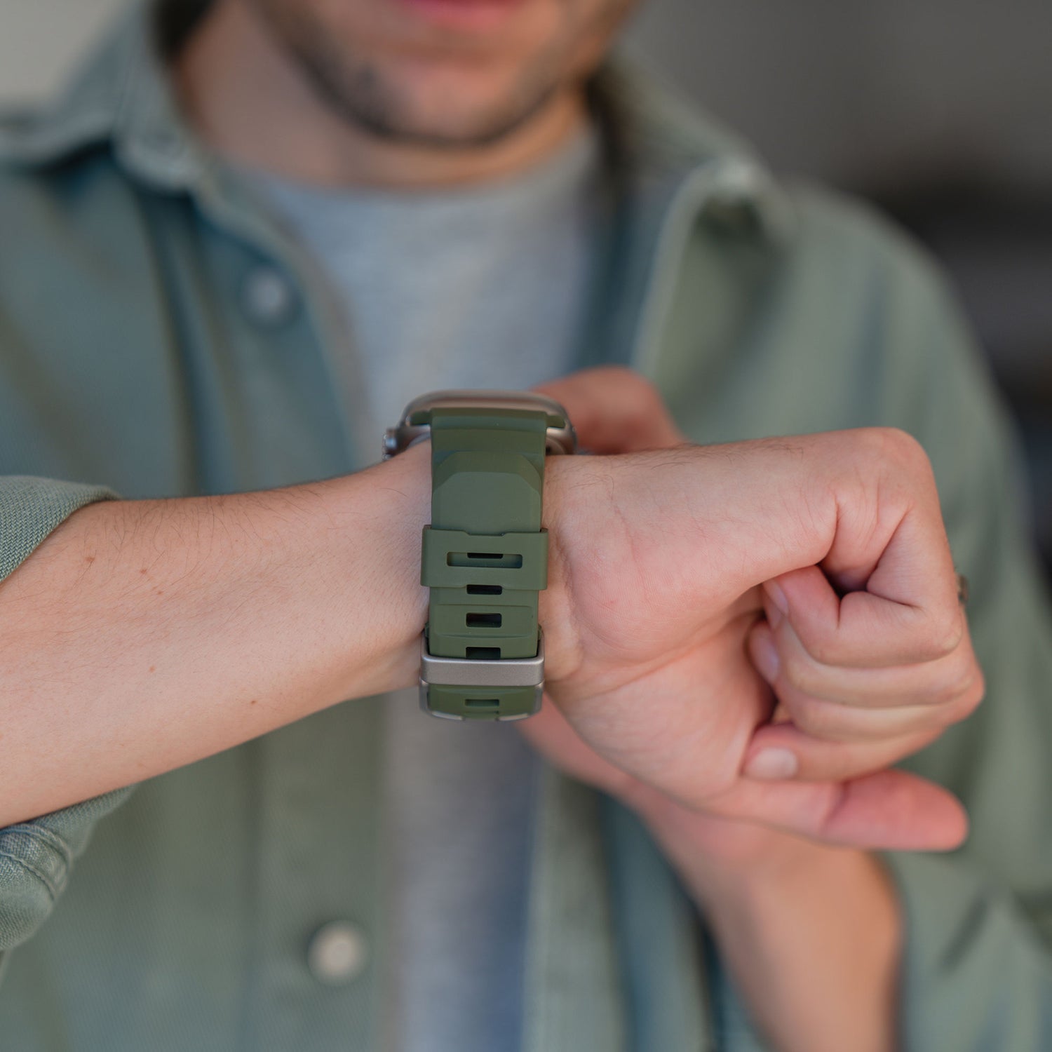 Eine Person trägt ein grünes Arktisband Apple Watch Armband "Flux" mit Edelstahl-Schließe und berührt ihr Handgelenk, während sie es ansieht.