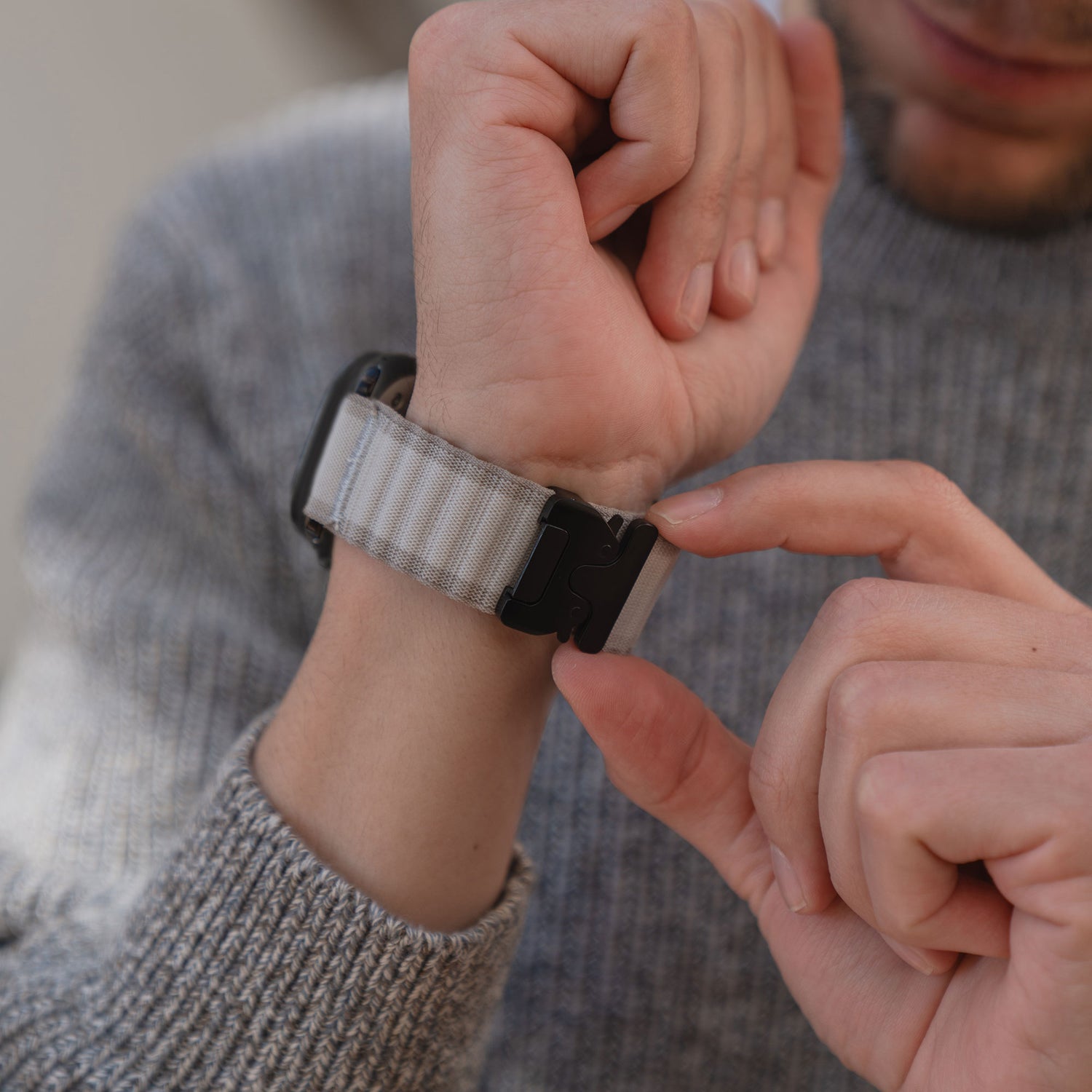 Eine Person, die ein graues Arktisband Apple Watch Armband "CoreX" an ihrem Handgelenk befestigt, während sie einen strukturierten grauen Pullover trägt.