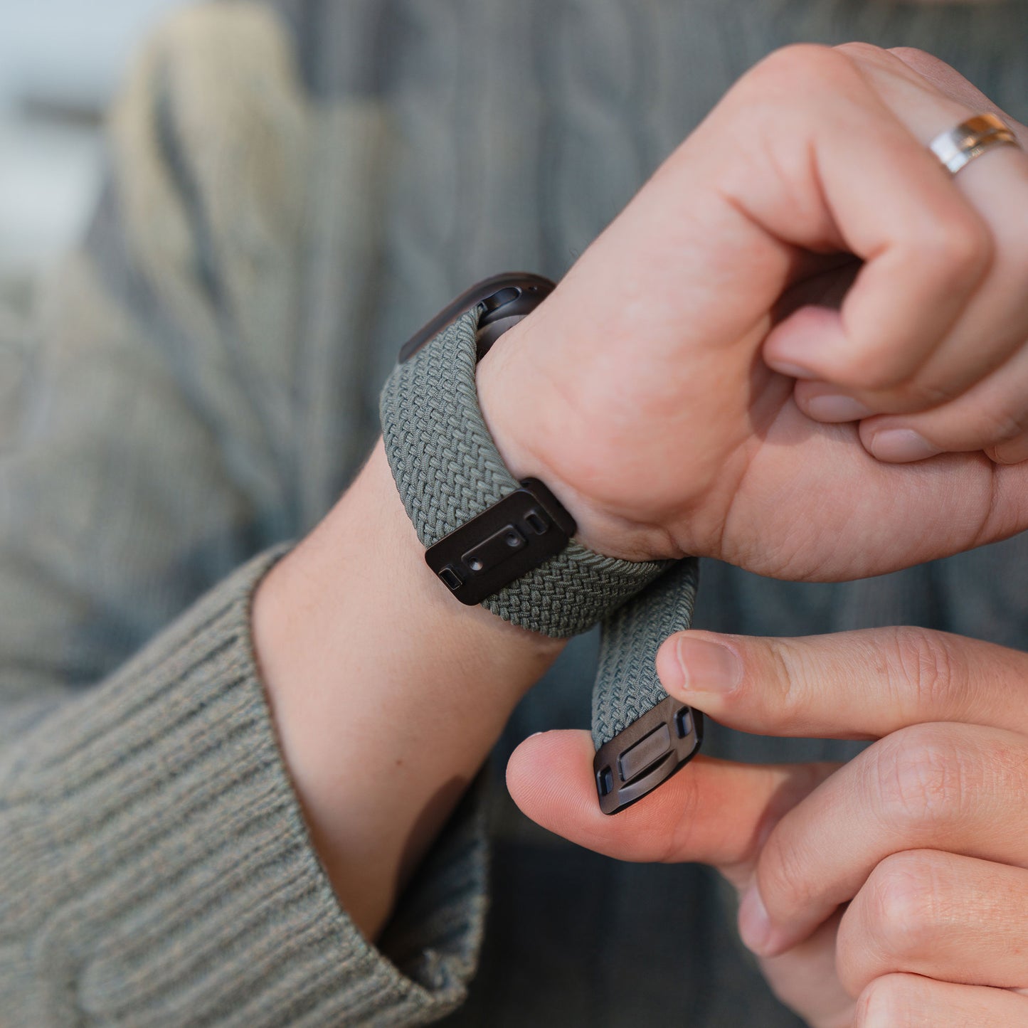 Eine Person, die das arktisband „Geflochtenes Apple Watch Ultra Armband ‚Casual‘“ mit Magnetverschluss in Grau am Handgelenk trägt, kombiniert mit einem grauen Strickpullover und einem Ring – eine ideale Wahl von arktisband, um Ihrer Apple Watch einen Hauch von subtiler Eleganz zu verleihen.