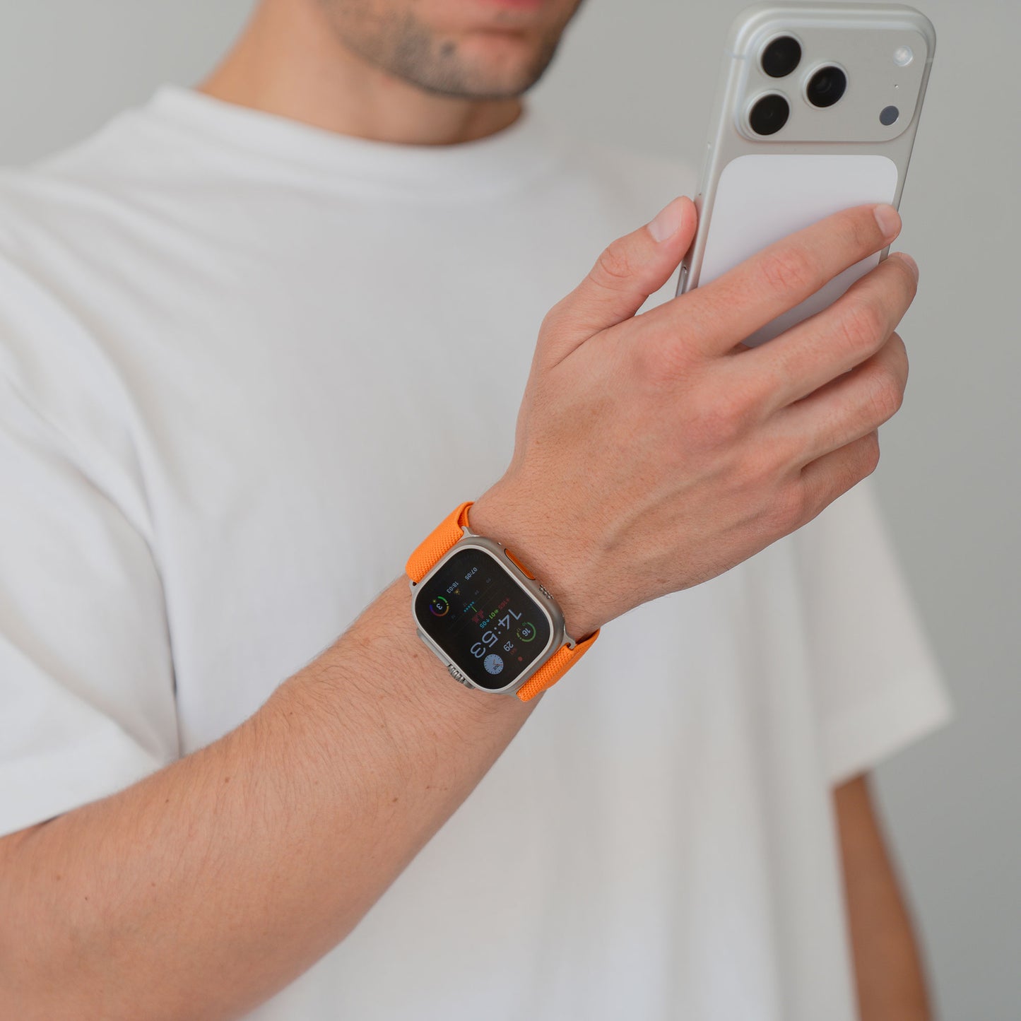 Person mit weißem Hemd, die ein Smartphone hält und ein Arktisband Apple Watch Nylonarmband "FlexOne" in Orange trägt.