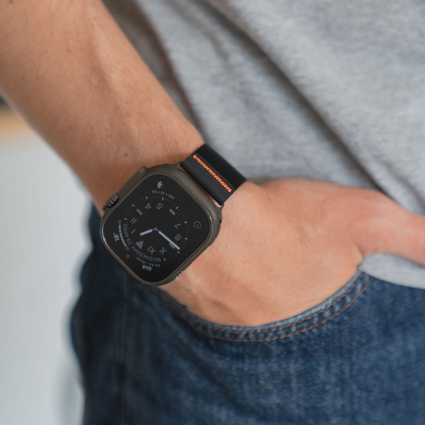 Eine Person, die das arktisband Apple Watch Armband "Terra" von arktisband mit einem schwarzen 24 mm extrabreiten Band trägt, Hand in der Tasche, bekleidet mit einem grauen Hemd und blauen Jeans.