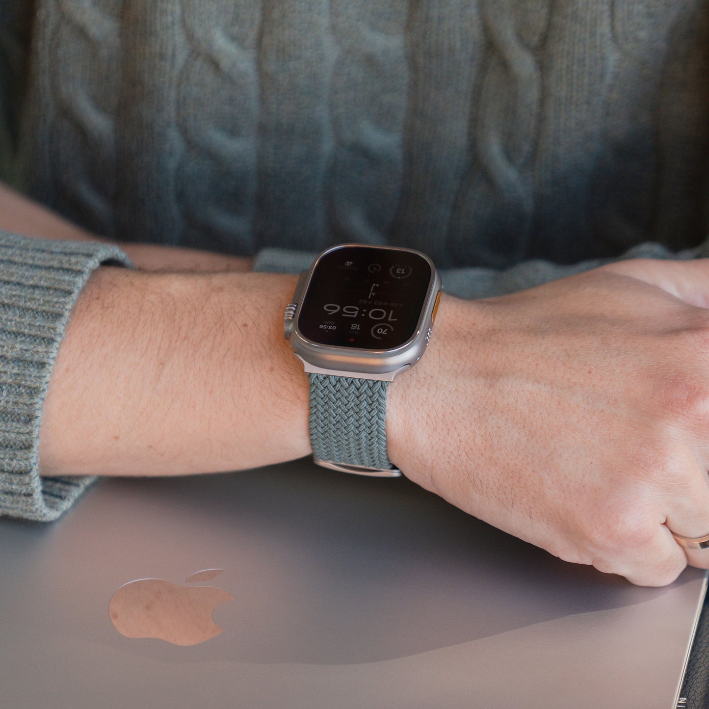 Eine Person, die ein „Geflochtenes“ Apple Watch Ultra-Armband „Casual“ von arktisband mit Magnetverschluss in Grau trägt, legt ihre Hand auf einen geschlossenen MacBook-Laptop.