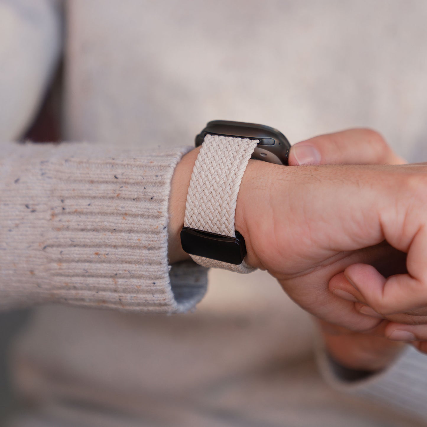 Eine Person, die ein „Geflochtenes“ Arktisband für die Apple Watch Ultra „Casual“ mit Magnetverschluss in Beige am Handgelenk trägt, passt es mit der anderen Hand an und befestigt es mit dem praktischen Magnetverschluss.