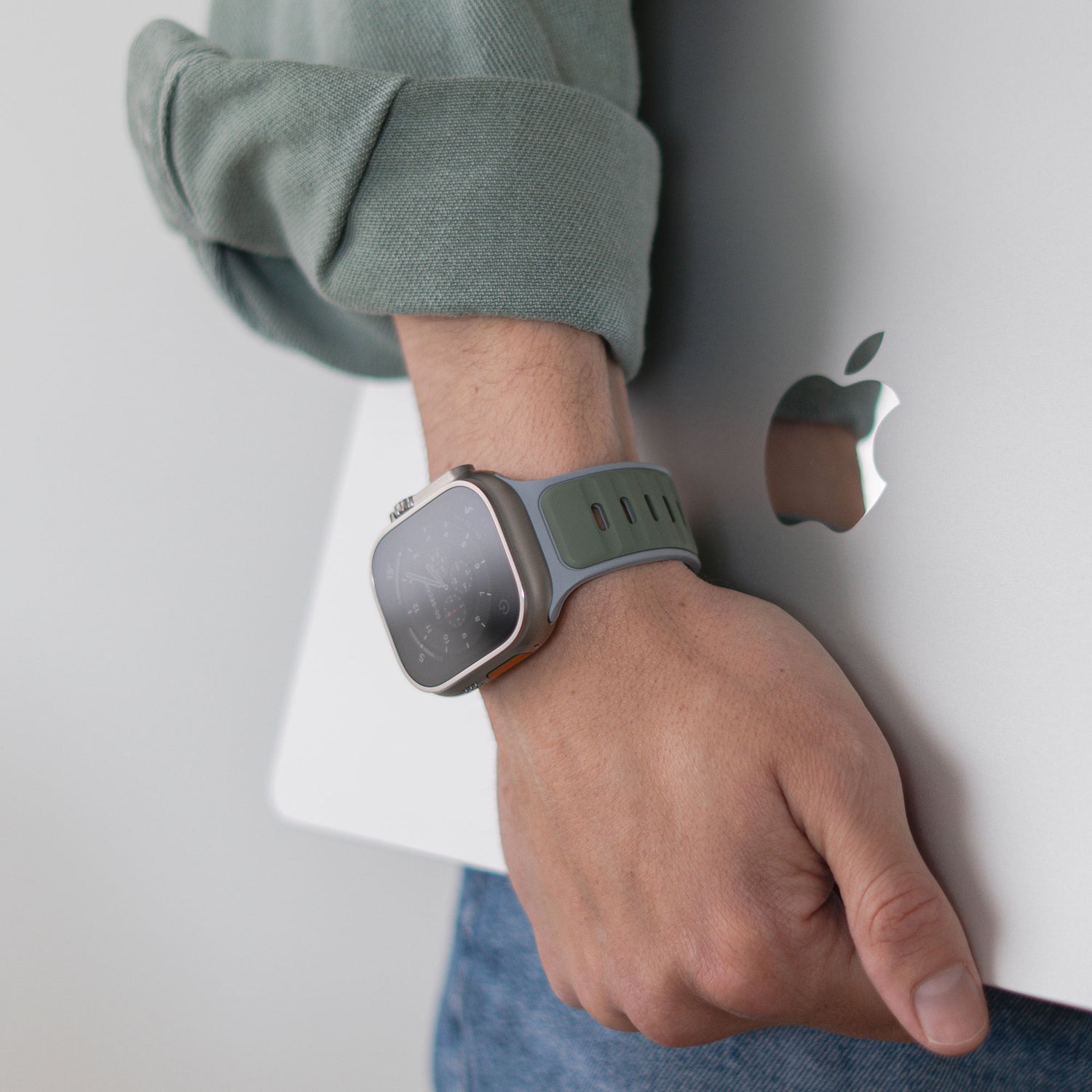 Eine Person, die ein Arktisband Apple Watch Silikonarmband „Swift“ trägt, hält ein silbernes MacBook mit sichtbarem Apple-Logo.