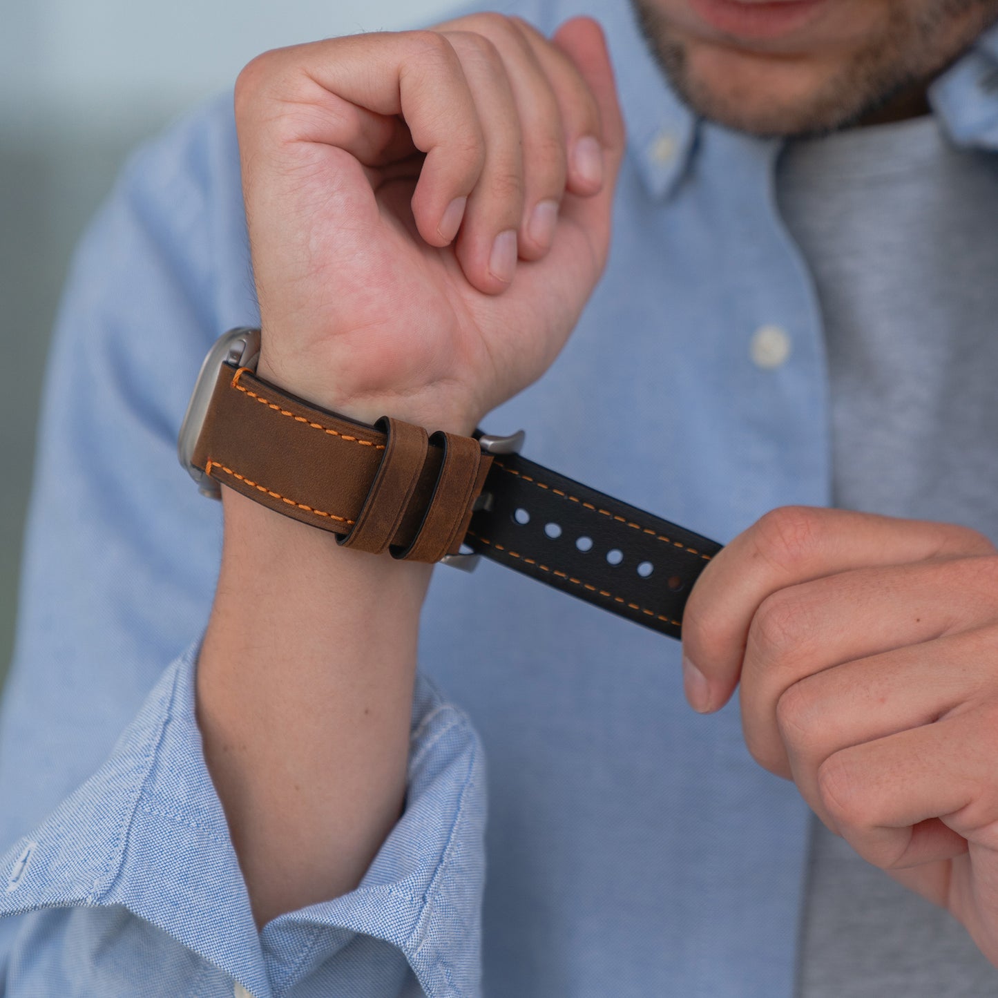 Ein Mann in einem blauen Hemd befestigt ein arktisband Apple Watch Ultra PALERMO GRANDE Lederarmband von arktisband mit einer 316L-Edelstahlschließe an seinem Handgelenk.