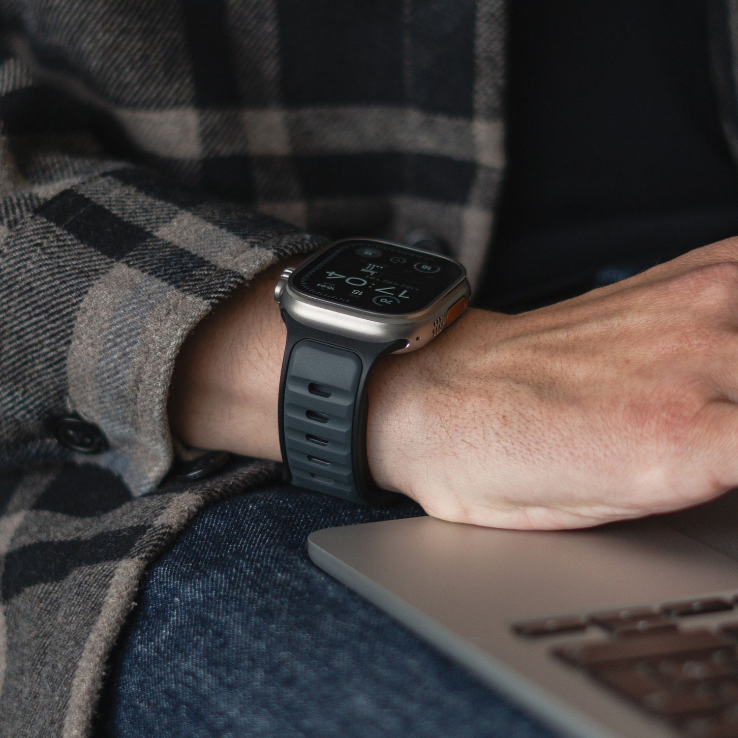 Eine Person in einem karierten Flanellhemd und Jeans trägt ein arktisband Apple Watch Silikonarmband „Swift“ und legt ihre Hand auf einen Laptop. Die schweißabsorbierende, atmungsaktive Qualität des artisband Silikonarmbands gewährleistet sportlichen Komfort.