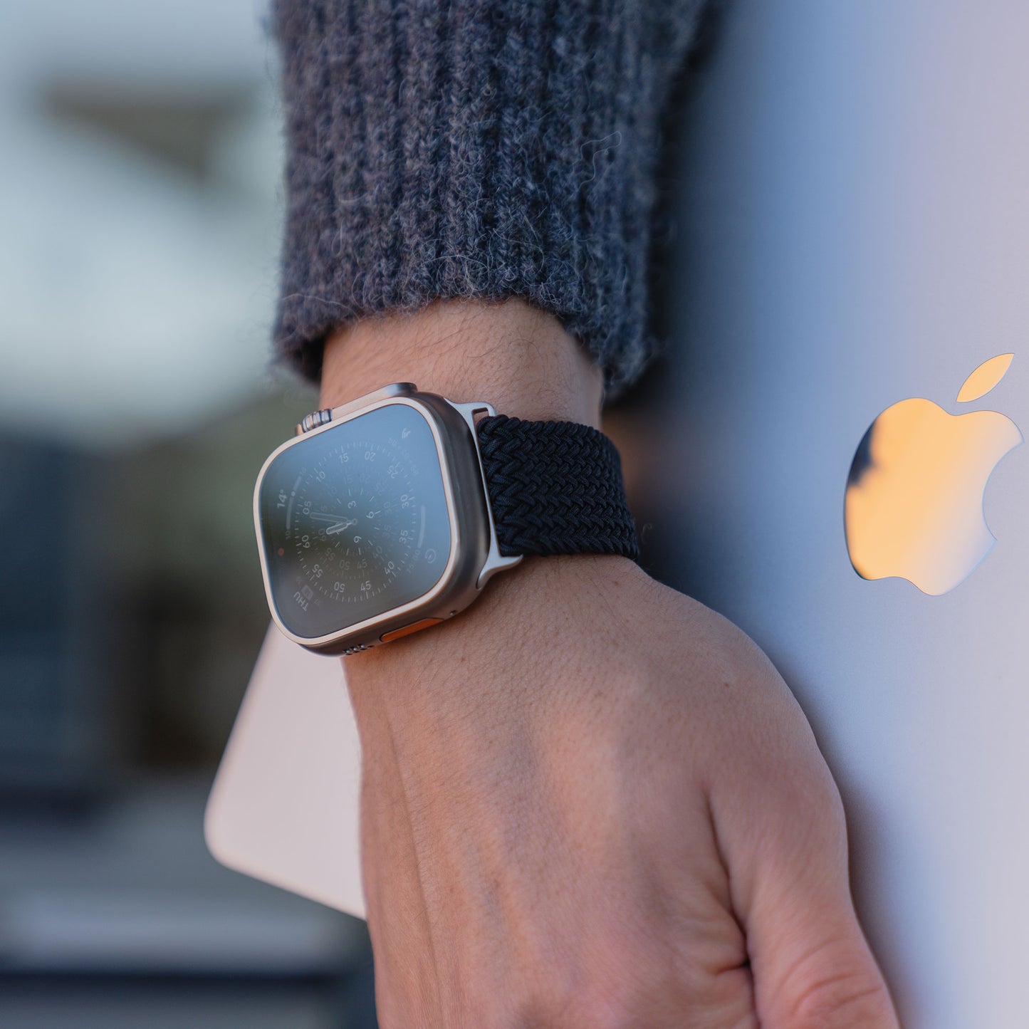 Eine Person, die ein „Geflochtenes“ Apple Watch Ultra-Armband „Casual“ von arktisband mit Magnetverschluss trägt, hält ein silbernes MacBook mit dem Apple-Logo in der Hand.