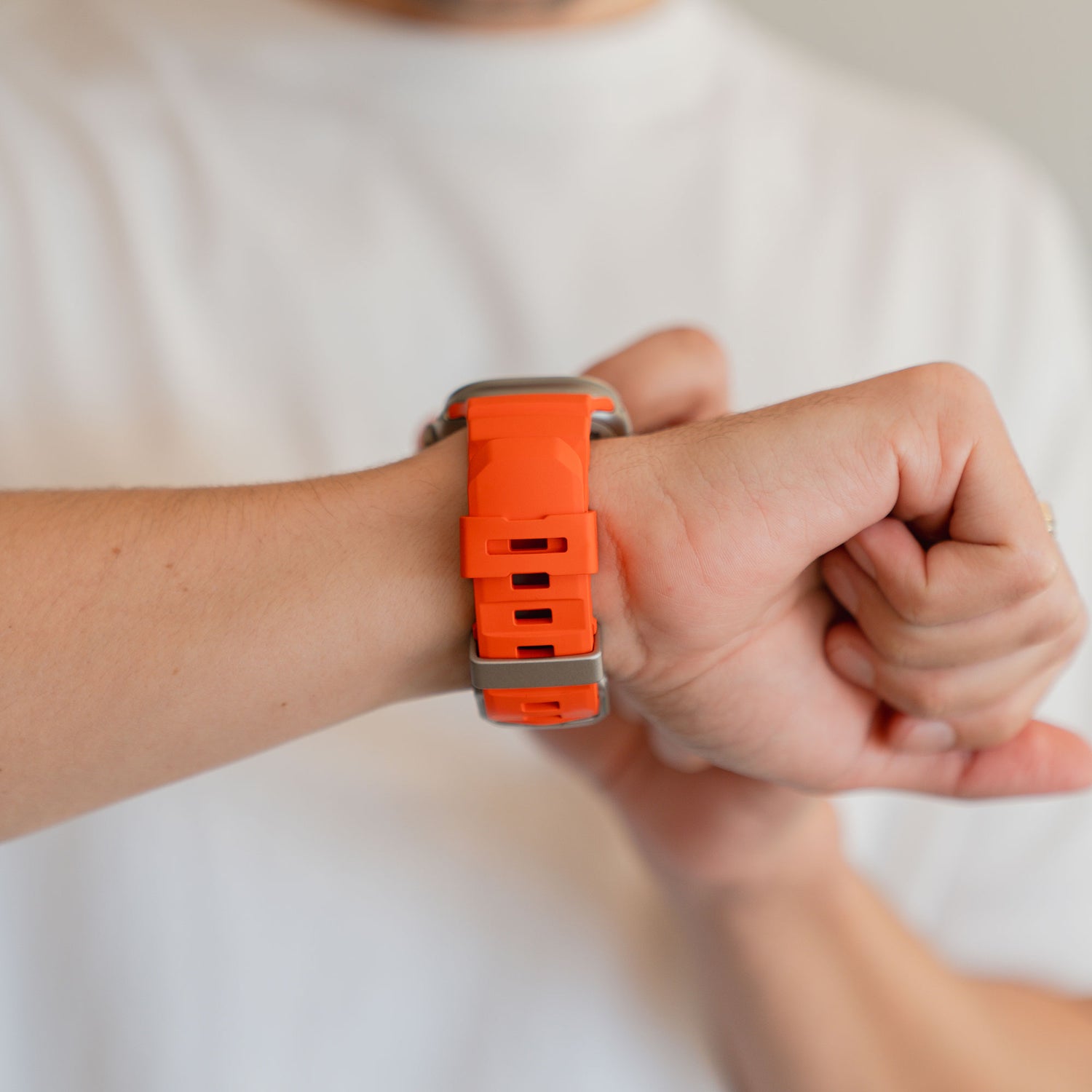 Eine Person mit einem arktisband Apple Watch Armband "Flux" in orange FKM und einer schlichten Edelstahl Schließe am Handgelenk, gepaart mit einem weißen Hemd.