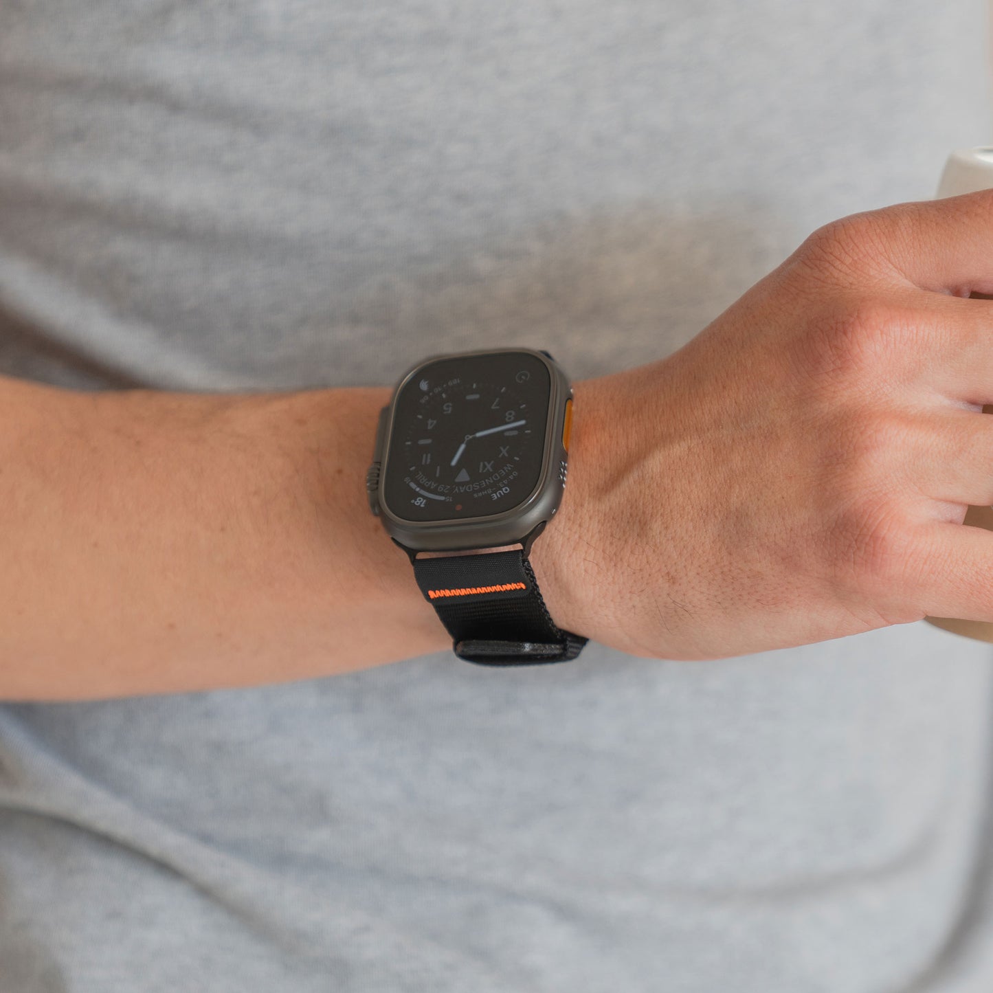 Eine Person, die das arktisband Apple Watch Armband "Terra" von arktisband mit einem schwarzen Outdoor-Nylonband trägt, hält eine Tasse und ist mit einem hellgrauen Hemd bekleidet.