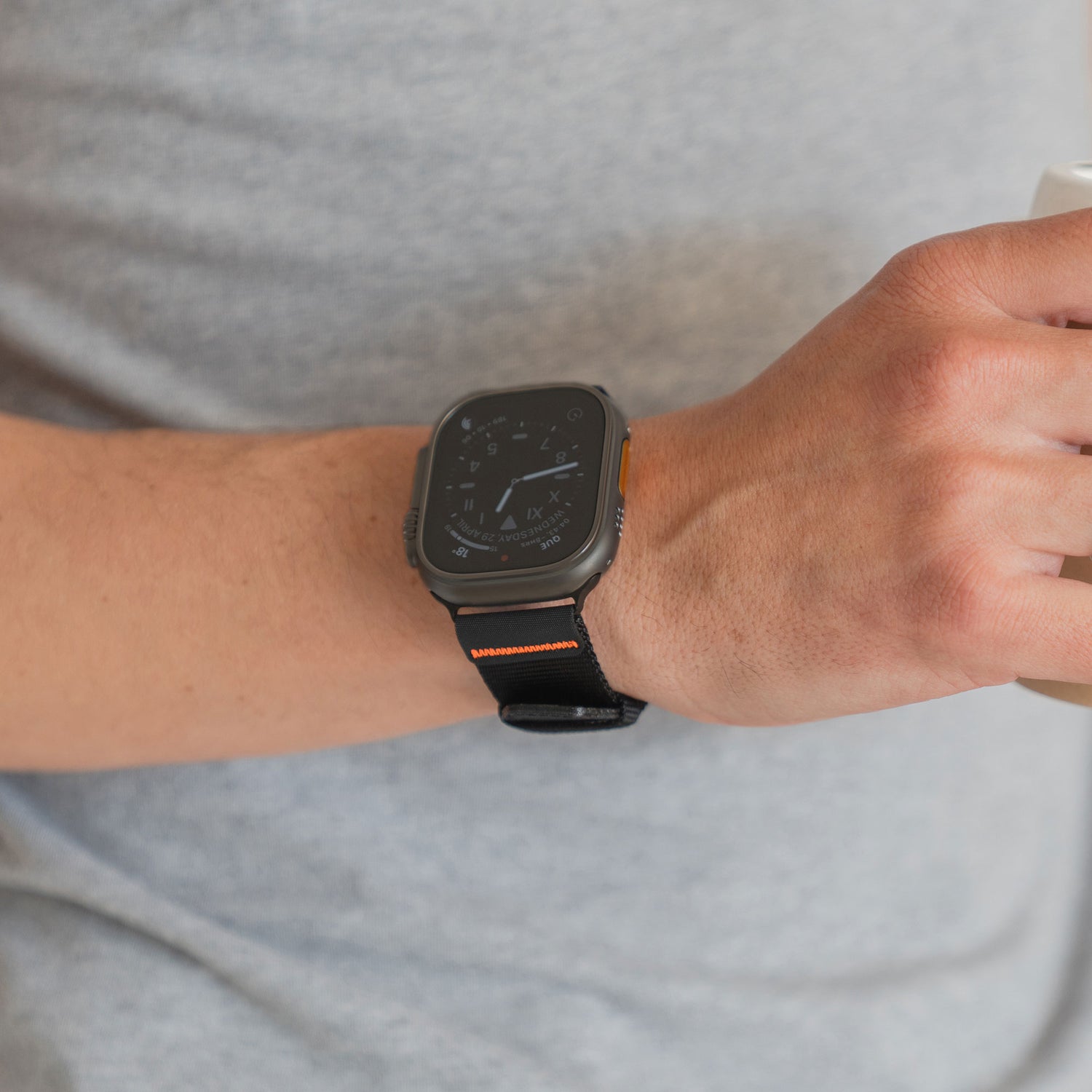 Eine Person, die das arktisband Apple Watch Armband "Terra" von arktisband mit einem schwarzen Outdoor-Nylonband trägt, hält eine Tasse und ist mit einem hellgrauen Hemd bekleidet.