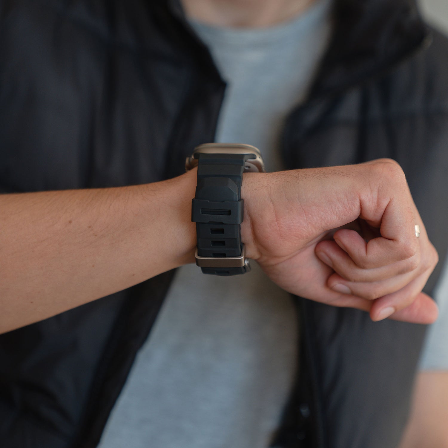 Eine Person in grauem Hemd und schwarzer Weste überprüft ihr arktisband Apple Watch Armband "Flux" an ihrem linken Handgelenk.