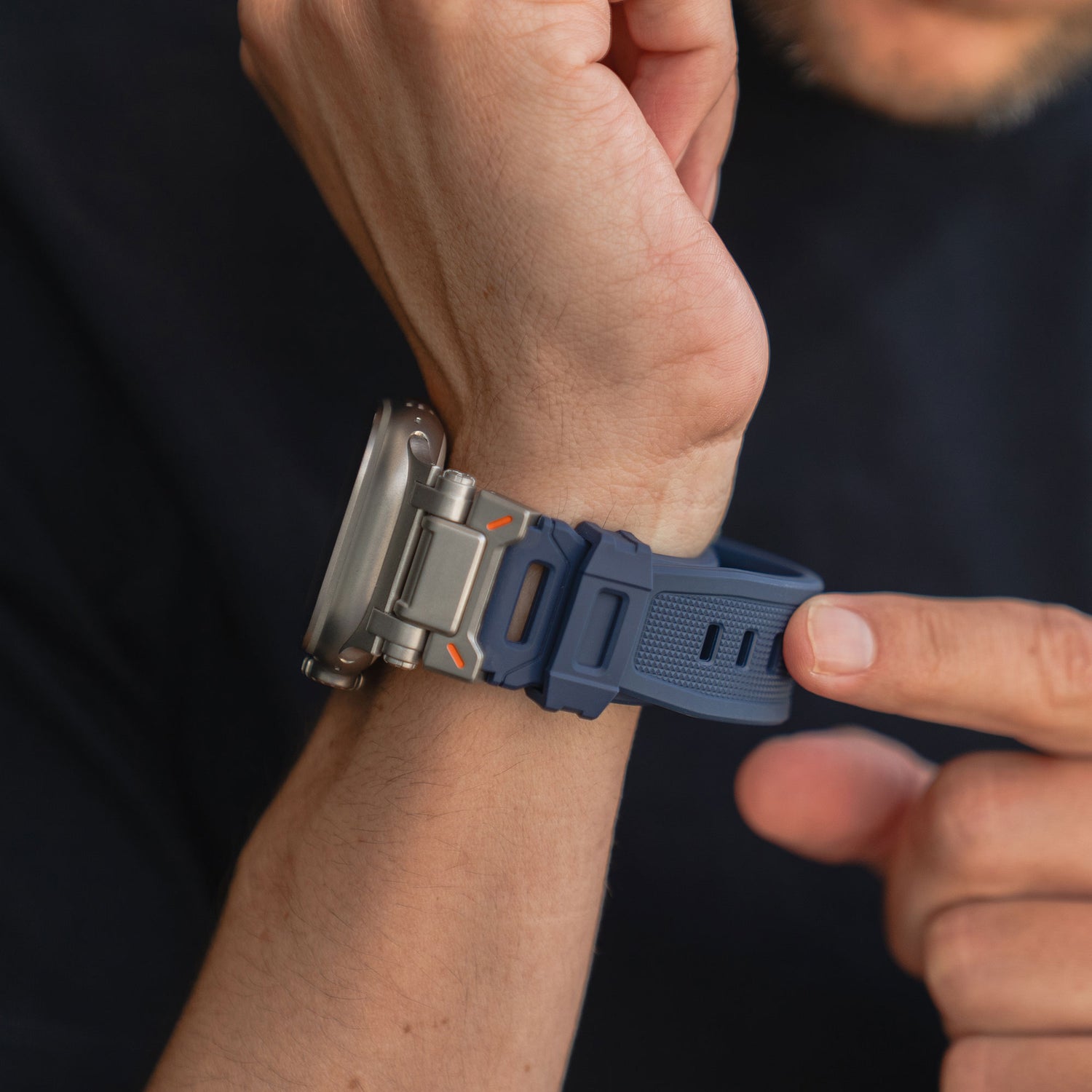 Eine Person befestigt ein Arktisband Apple Watch Ultra Armband „Atlas“ in Blau an ihrem linken Handgelenk und passt den Verschluss mit der rechten Hand an, während das Zifferblatt der Apple Watch Ultra teilweise sichtbar ist.