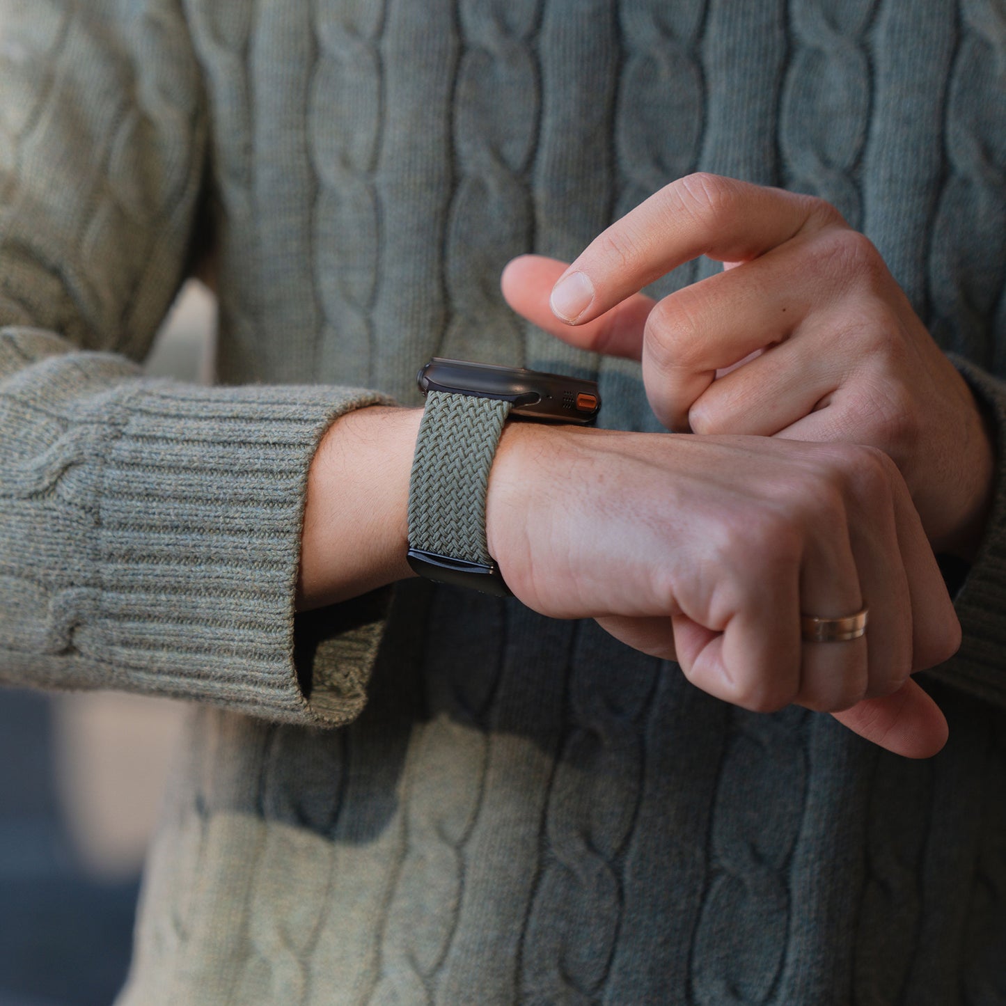 Eine Person in einem grünen Pullover trägt am linken Handgelenk eine Smartwatch mit dem „Casual“-Armband „Geflochtenes Apple Watch Ultra“-Armband von arktisband mit Magnetverschluss.