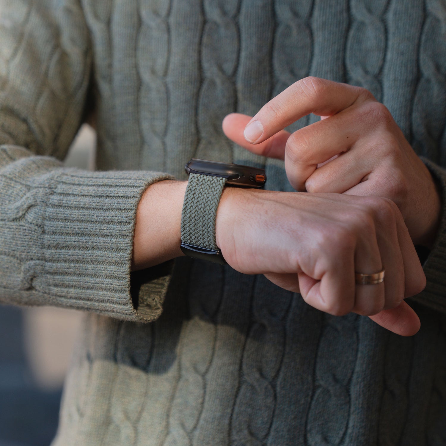 Eine Person in einem grünen Pullover trägt am linken Handgelenk eine Smartwatch mit dem „Casual“-Armband „Geflochtenes Apple Watch Ultra“-Armband von arktisband mit Magnetverschluss.