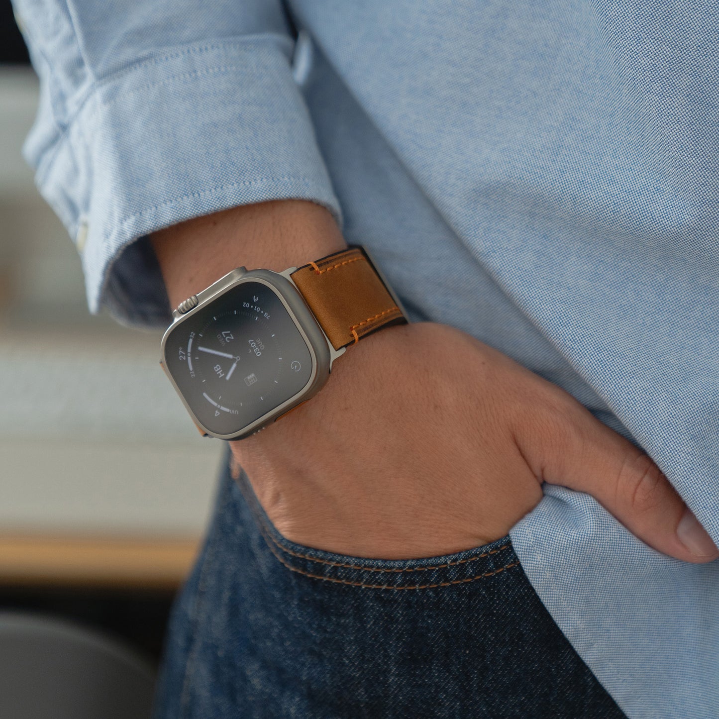 Nahaufnahme einer Person, die das Arktisband Apple Watch Ultra PALERMO GRANDE Lederarmband mit einer 316L-Edelstahlschließe trägt, gepaart mit einem braunen Lederarmband und einem hellblauen Hemd.