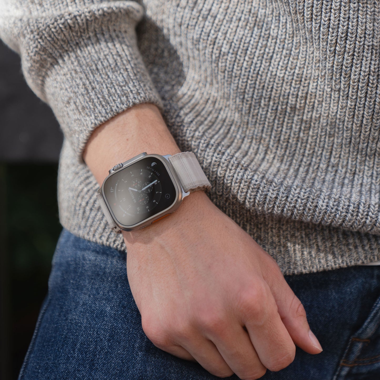 Eine Person in grauem Pullover und Jeans trägt das arktisband Apple Watch Armband "CoreX" mit Nylonband und Parachute-Verschluss von arktisband am Handgelenk.