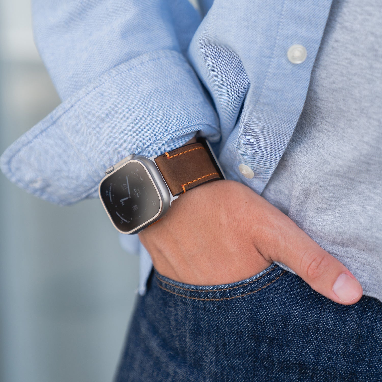 Eine Person trägt ein arktisband Apple Watch Ultra PALERMO GRANDE Lederarmband von arktisband, gefertigt aus hochwertigem Leder mit 316L-Edelstahl, Hand in der Jeanstasche, gepaart mit einem hellblauen Hemd.