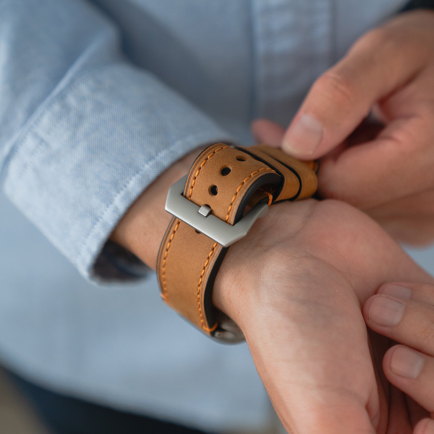 Eine Person befestigt ein Arktisband Apple Watch Ultra PALERMO GRANDE Lederarmband an ihrer Apple Watch und trägt ein blaues Hemd.