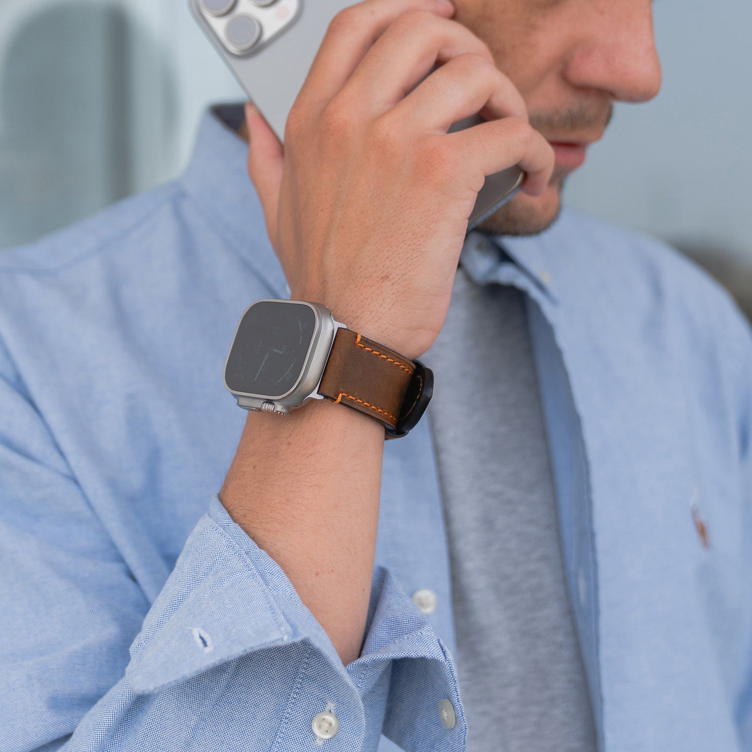 Ein Mann im blauen Hemd, der mit seinem Smartphone spricht, trägt eine Apple Watch Ultra mit dem arktisband PALERMO GRANDE Lederarmband von arktisband.