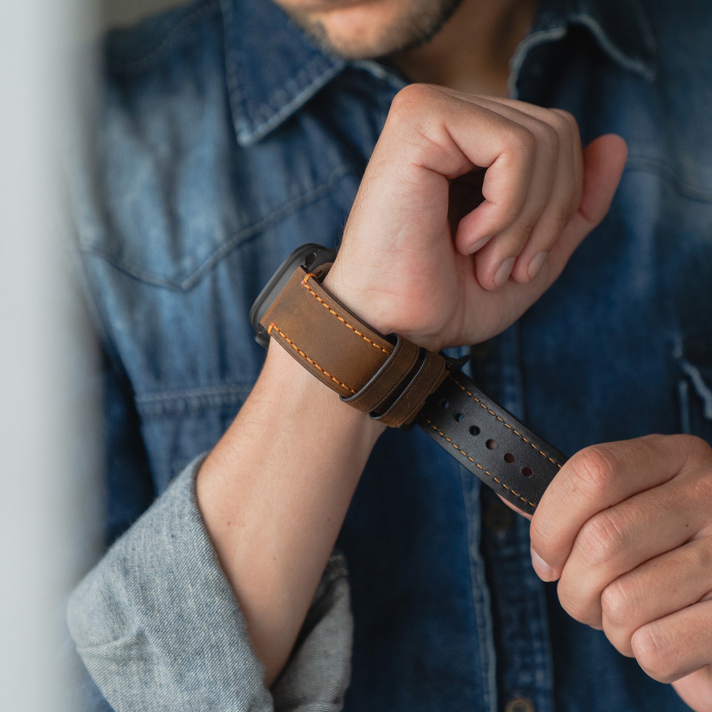 Eine Person in einem Jeanshemd legt sich ein arktisband Apple Watch Ultra PALERMO GRANDE Lederarmband von arktisband um das Handgelenk.