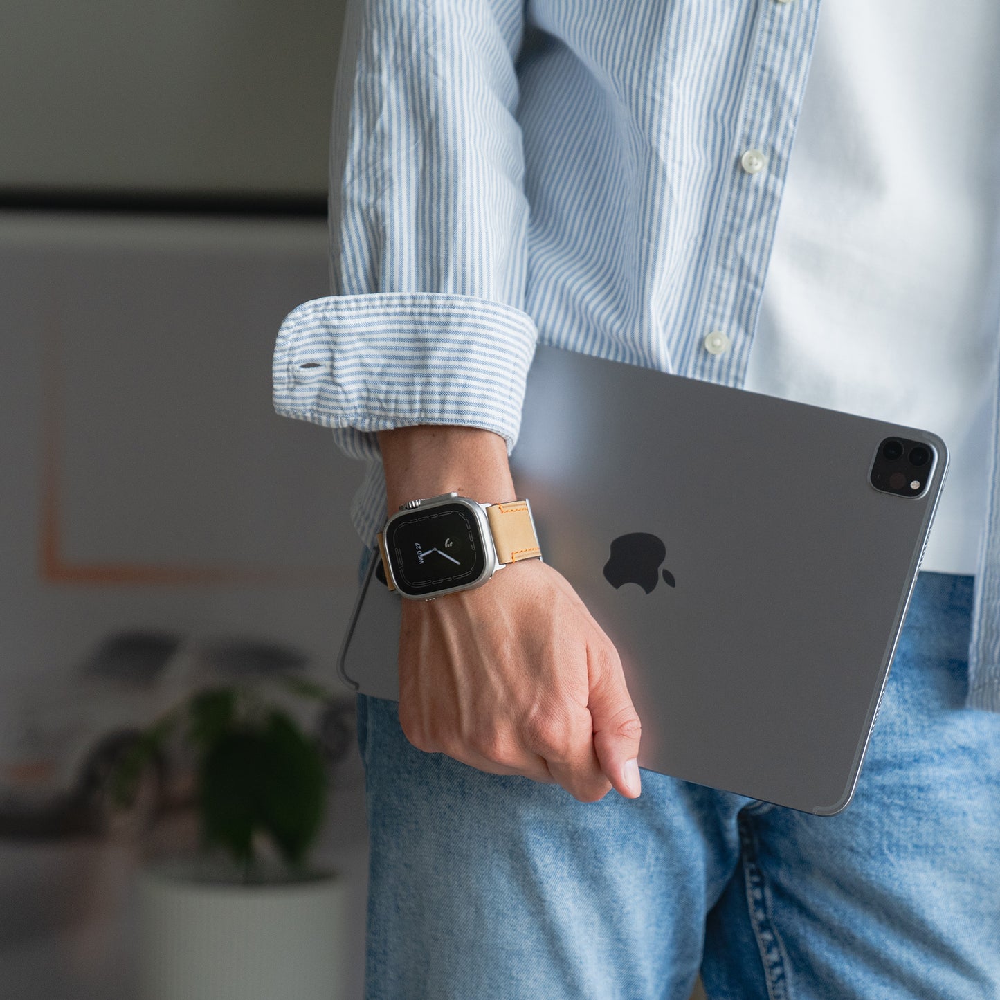 Eine Person im gestreiften Hemd hält ein iPad und trägt am linken Handgelenk ein arktisband Apple Watch Ultra PALERMO GRANDE Lederarmband mit einer robusten 316L-Edelstahlschließe.