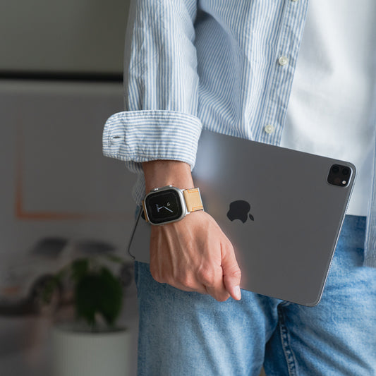 Eine Person im gestreiften Hemd hält ein iPad und trägt am linken Handgelenk ein arktisband Apple Watch Ultra PALERMO GRANDE Lederarmband mit einer robusten 316L-Edelstahlschließe.