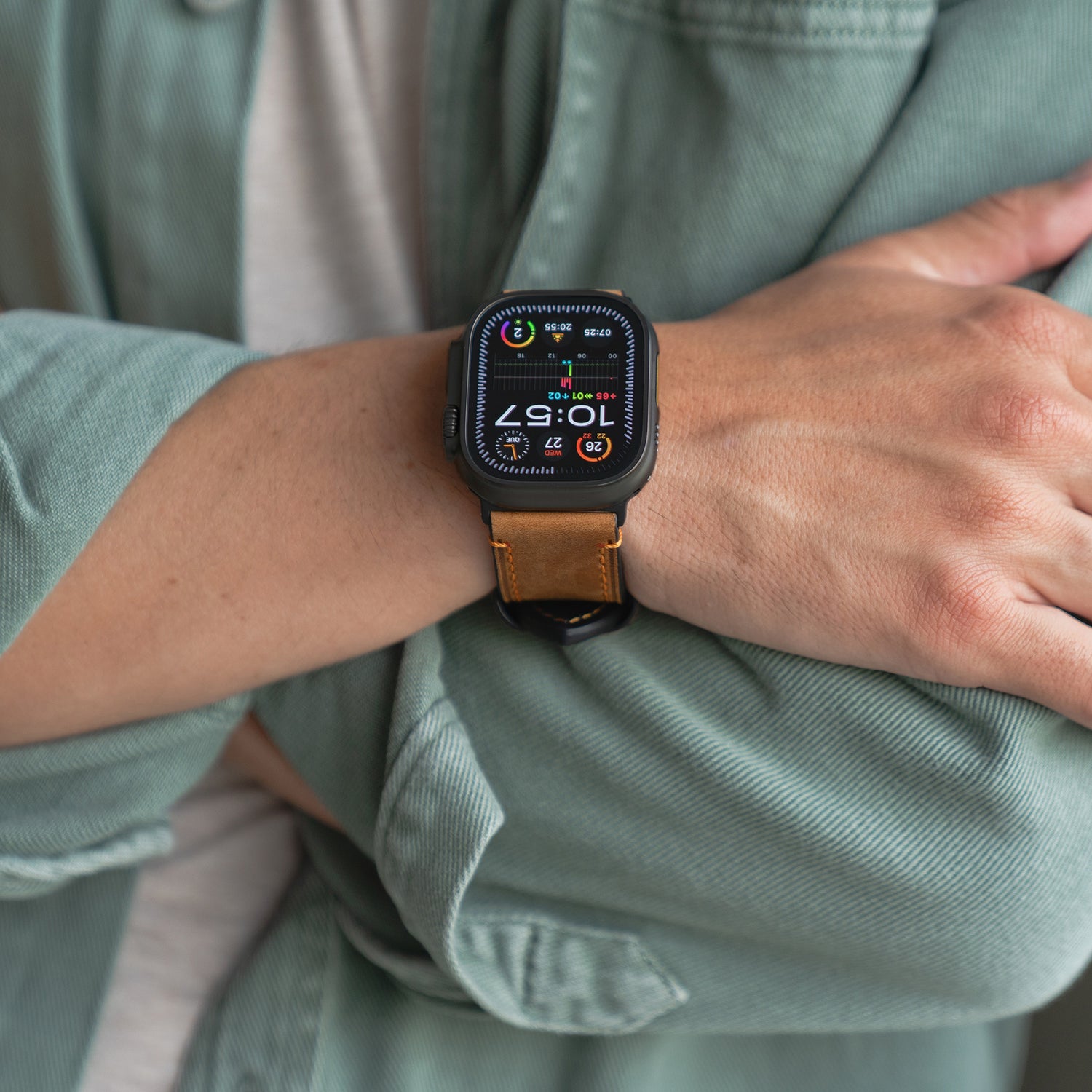 Eine Person trägt mit verschränkten Armen das Arktisband Apple Watch Ultra PALERMO GRANDE Lederarmband mit 316L-Edelstahl-Akzenten und einem leuchtenden Display.