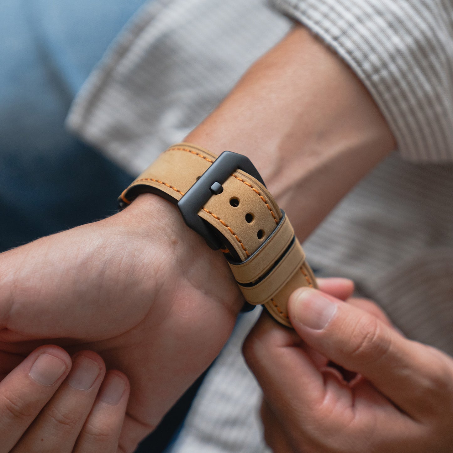 Das Arktisband Apple Watch Ultra PALERMO GRANDE Lederarmband mit 316L-Edelstahlschließe wird von einer Person mit beiden Händen am Handgelenk befestigt.