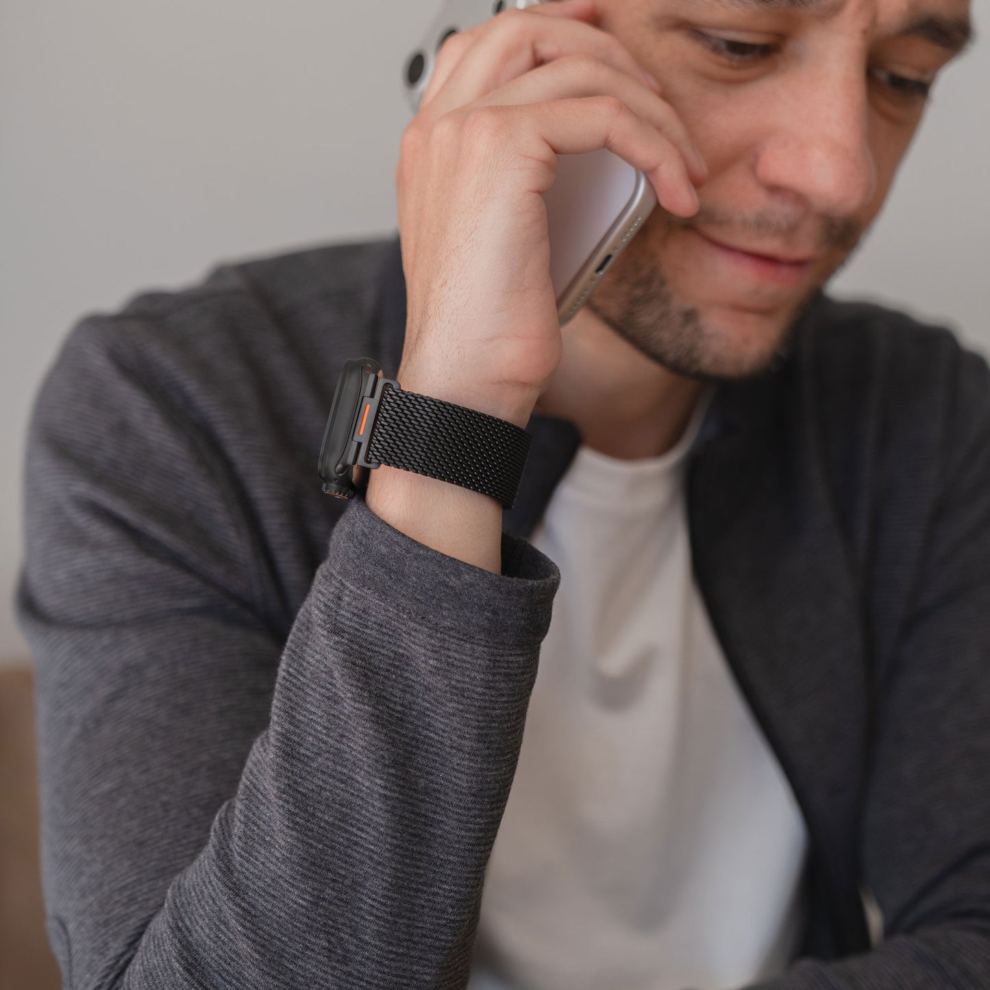 Ein Mann in grauer Jacke und weißem Hemd trägt eine Apple Watch Milanaise Armband "Bold SE" von arktisband und telefoniert mit einem Smartphone.