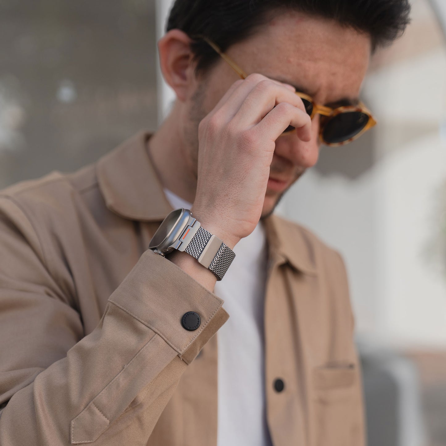Mann in beiger Jacke mit Sonnenbrille, trägt ein Arktisband Apple Watch Milanaise Armband "Bold SE" mit Magnetverschluss am Handgelenk.